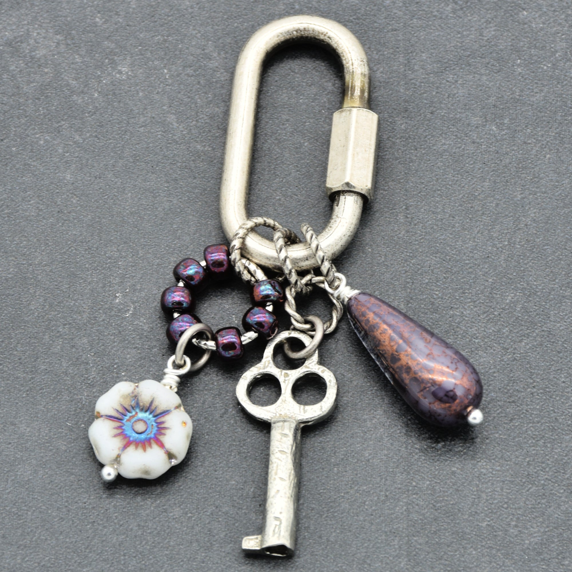 Keychain with various charms including a key, flower, and purple bead on a gray background