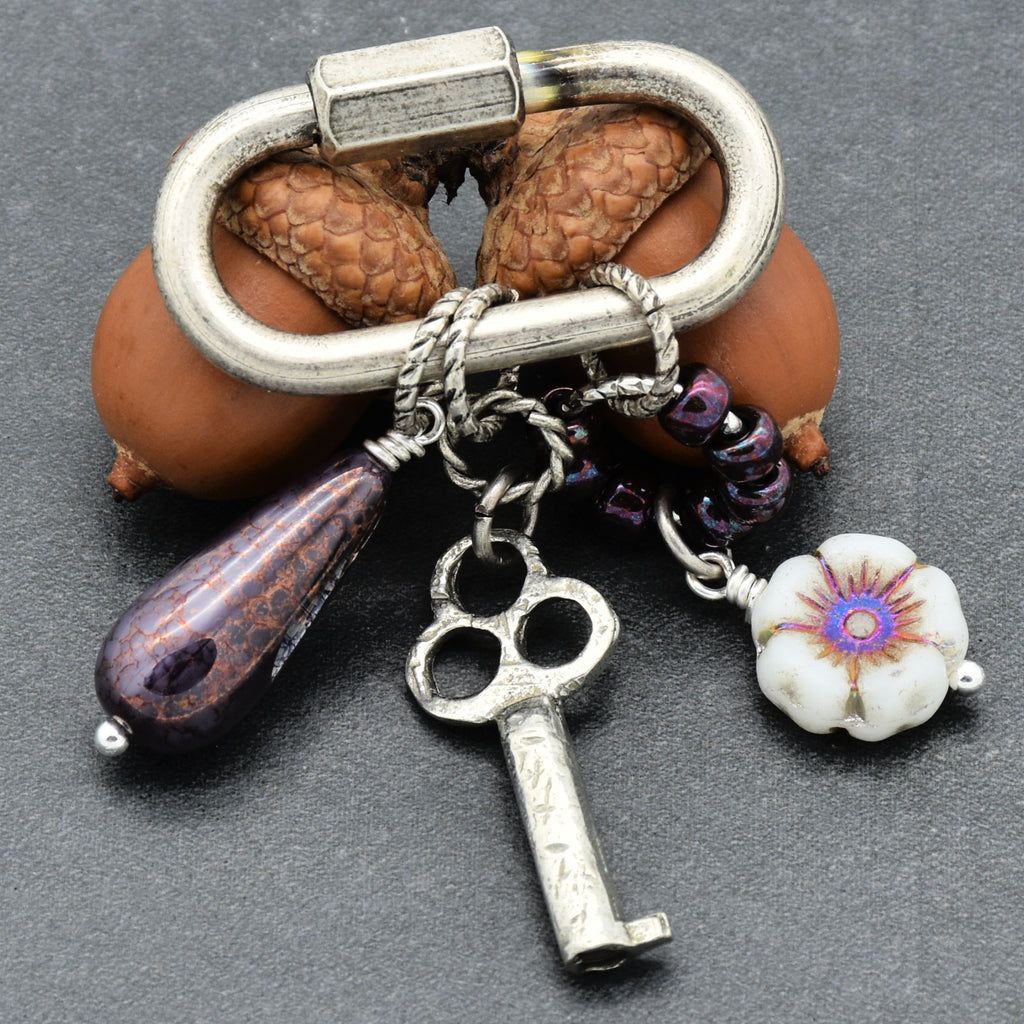 Keychain with charms including a key, flower, and a purple teardrop on a dark background