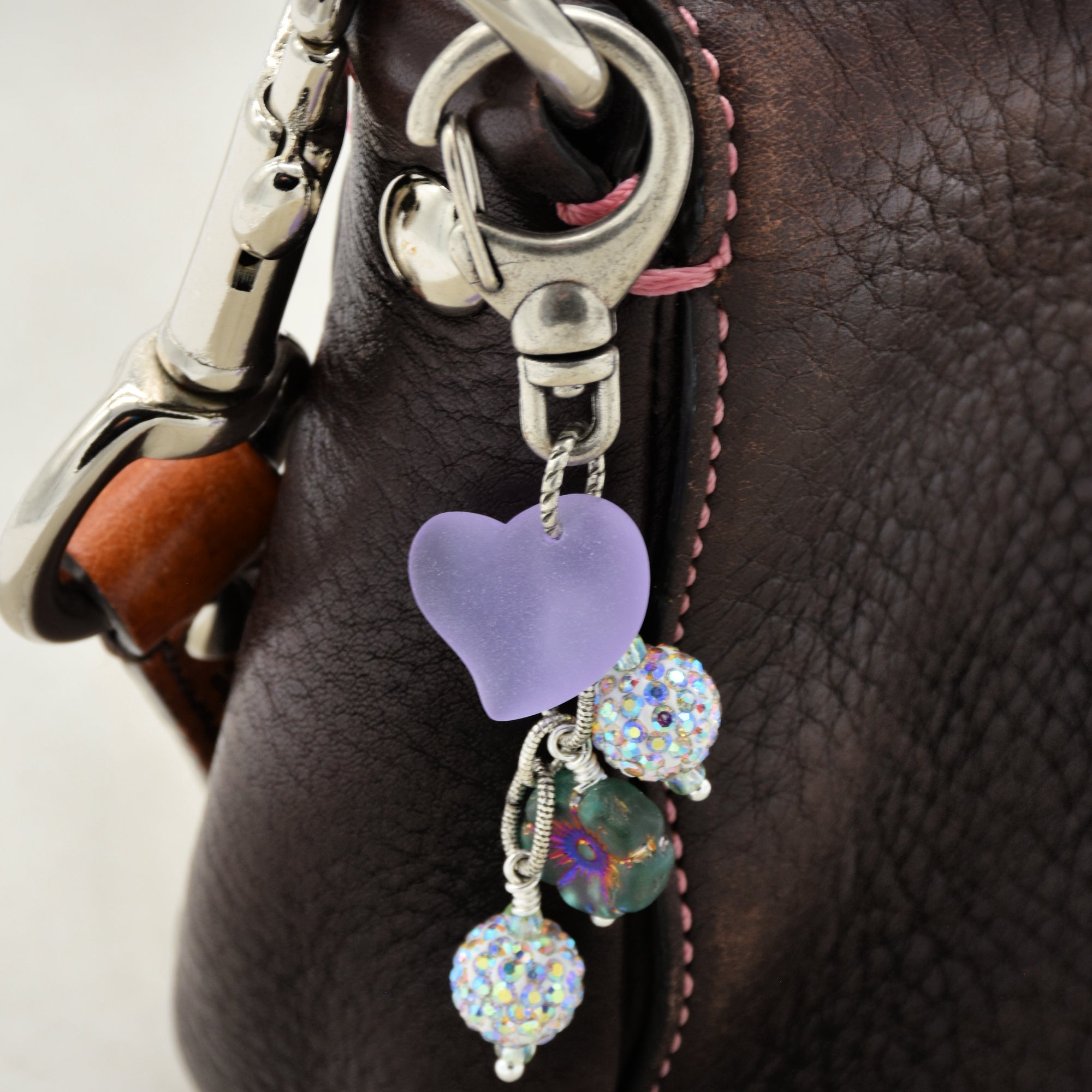 Close-up of a purple heart-shaped keychain with beads on a leather bag.