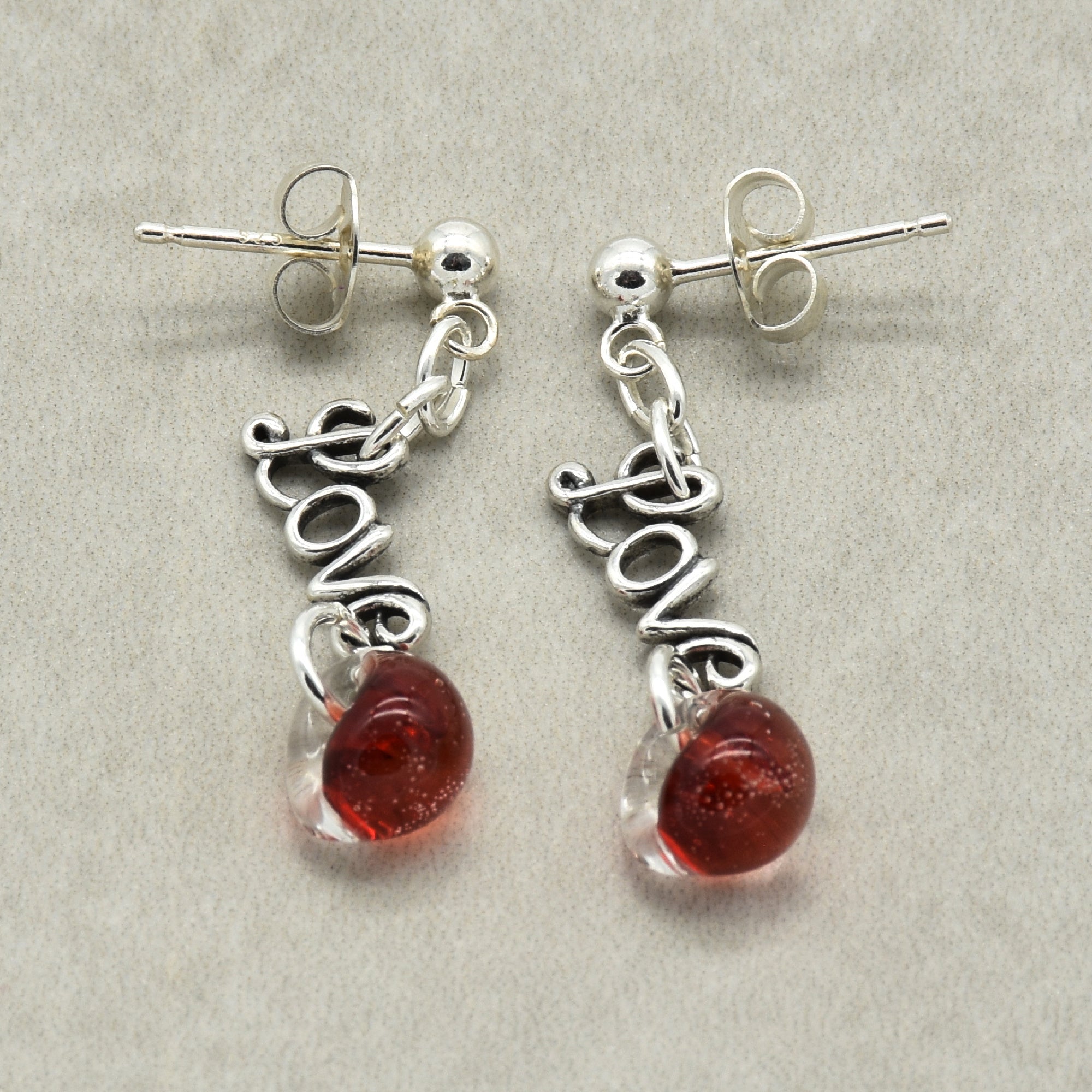Silver earrings with 'love' charms and red beads on a gray background