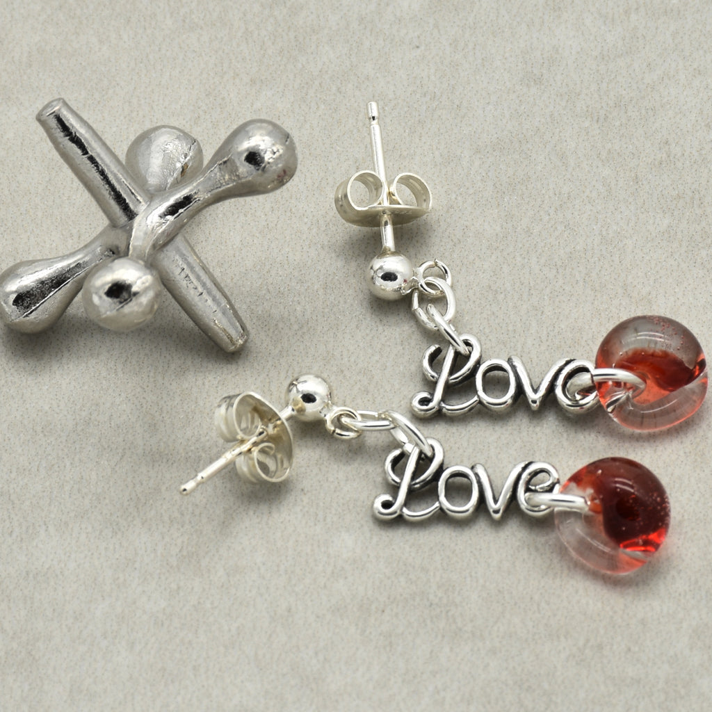 Silver earrings with 'Love' charms and red glass beads on a gray background