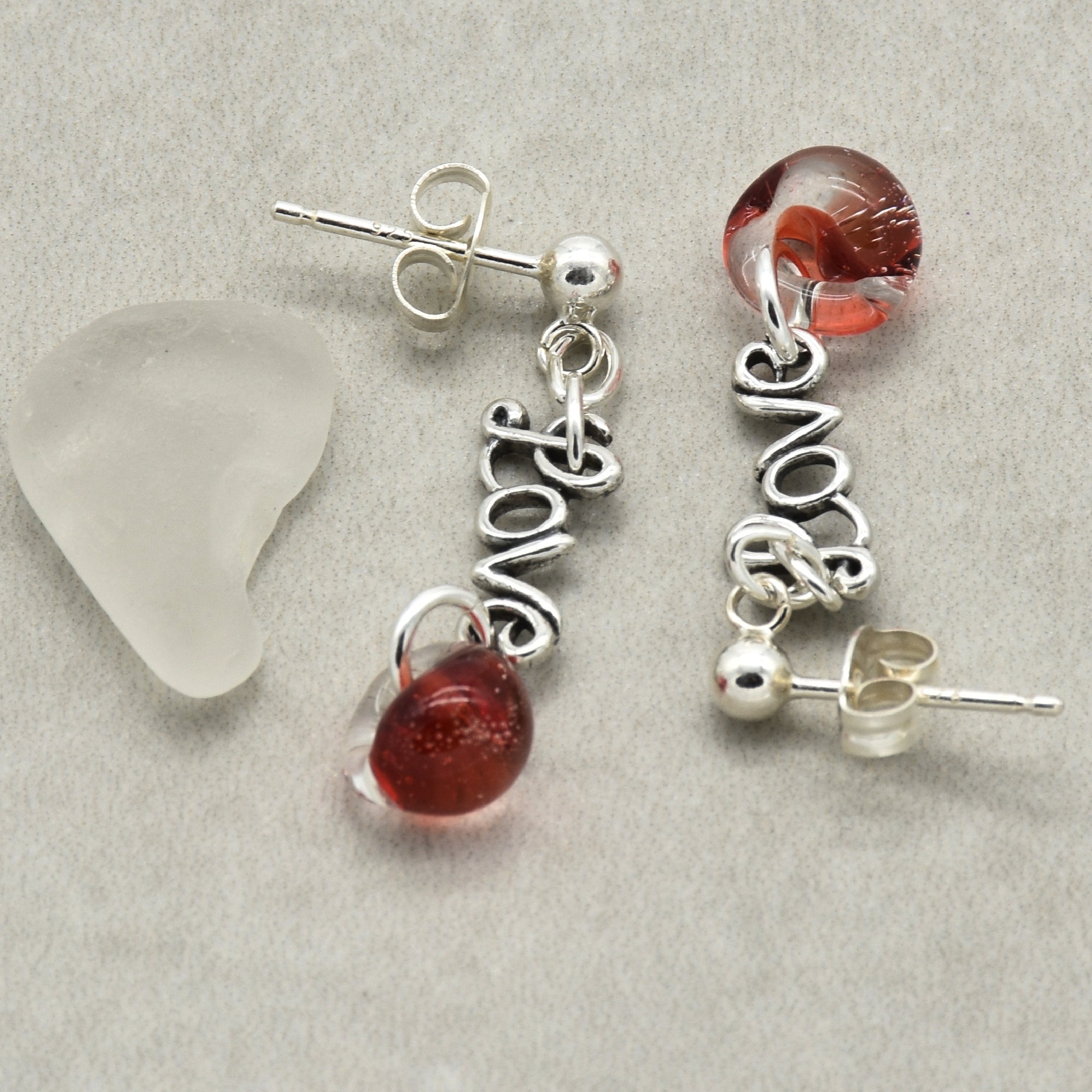 Silver earrings with 'love' charms and red beads on a gray surface.