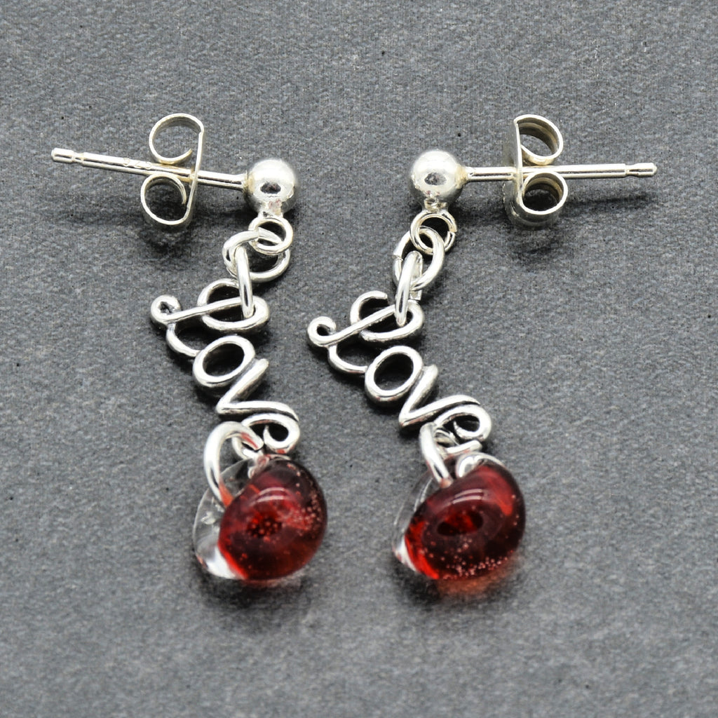 Silver earrings with 'love' and red glass charms on a gray background
