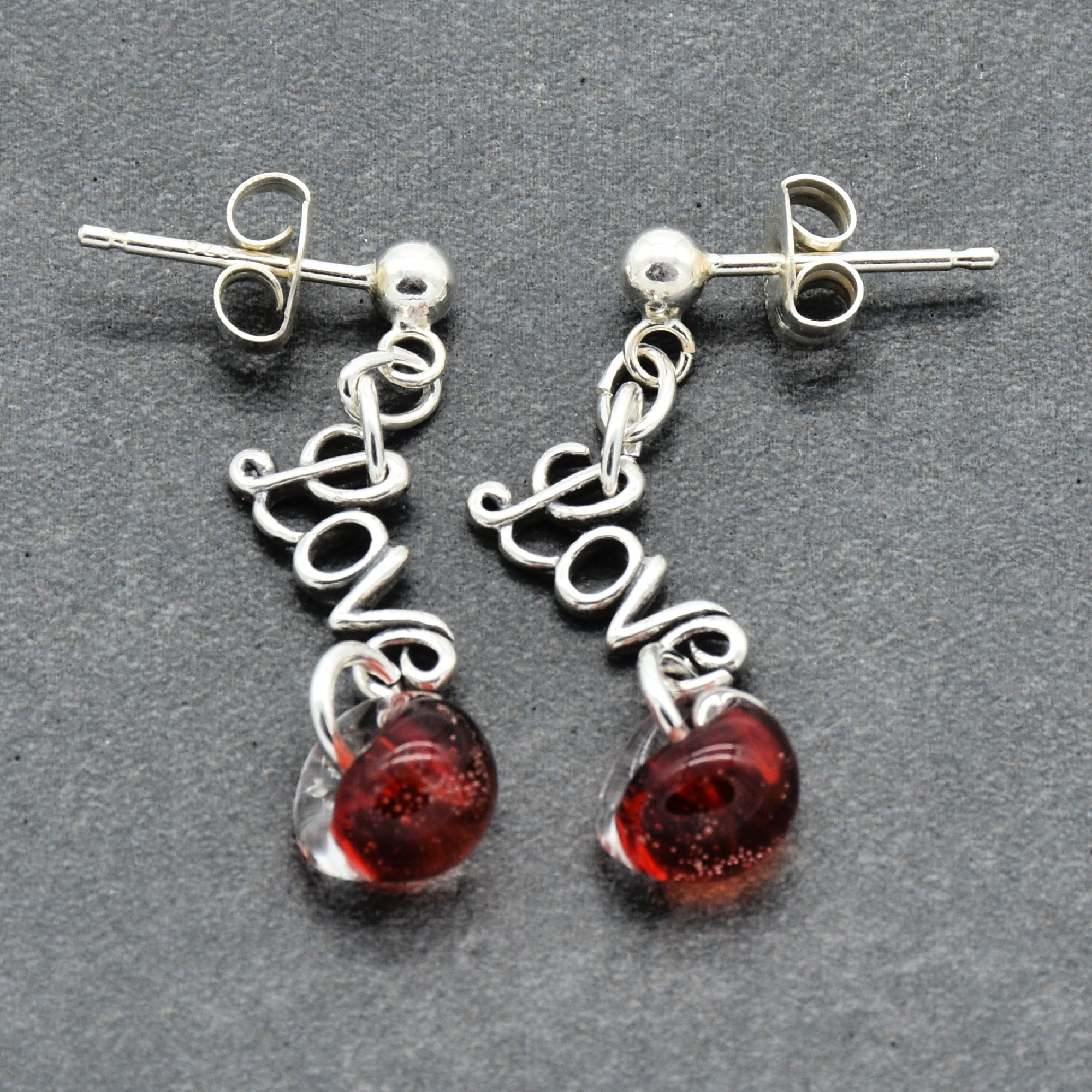 Silver earrings with 'love' and red glass charms on a gray background