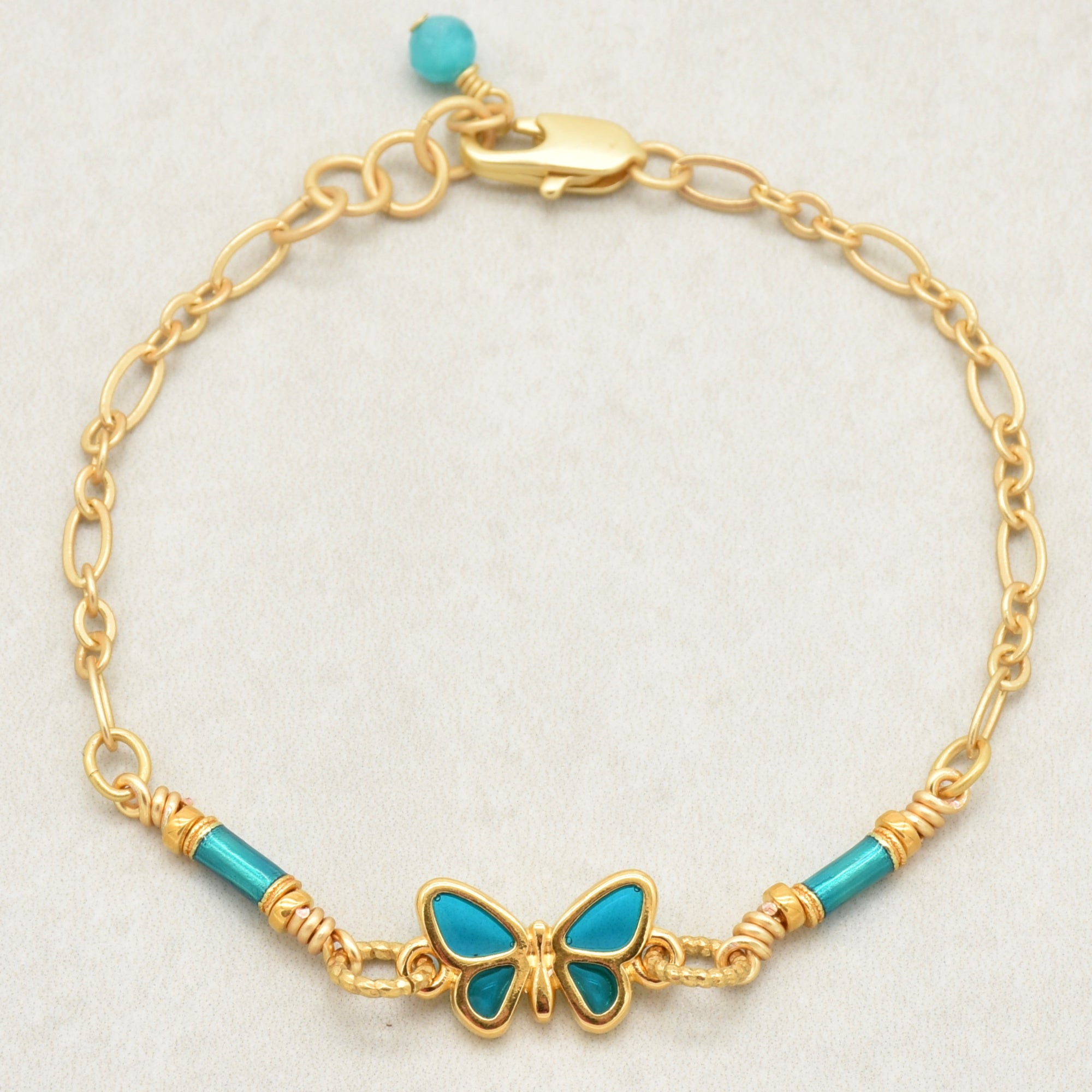 Gold bracelet with turquoise beads and butterfly charm on a light gray background - tell your story with art you can wear by Ruby Acorn