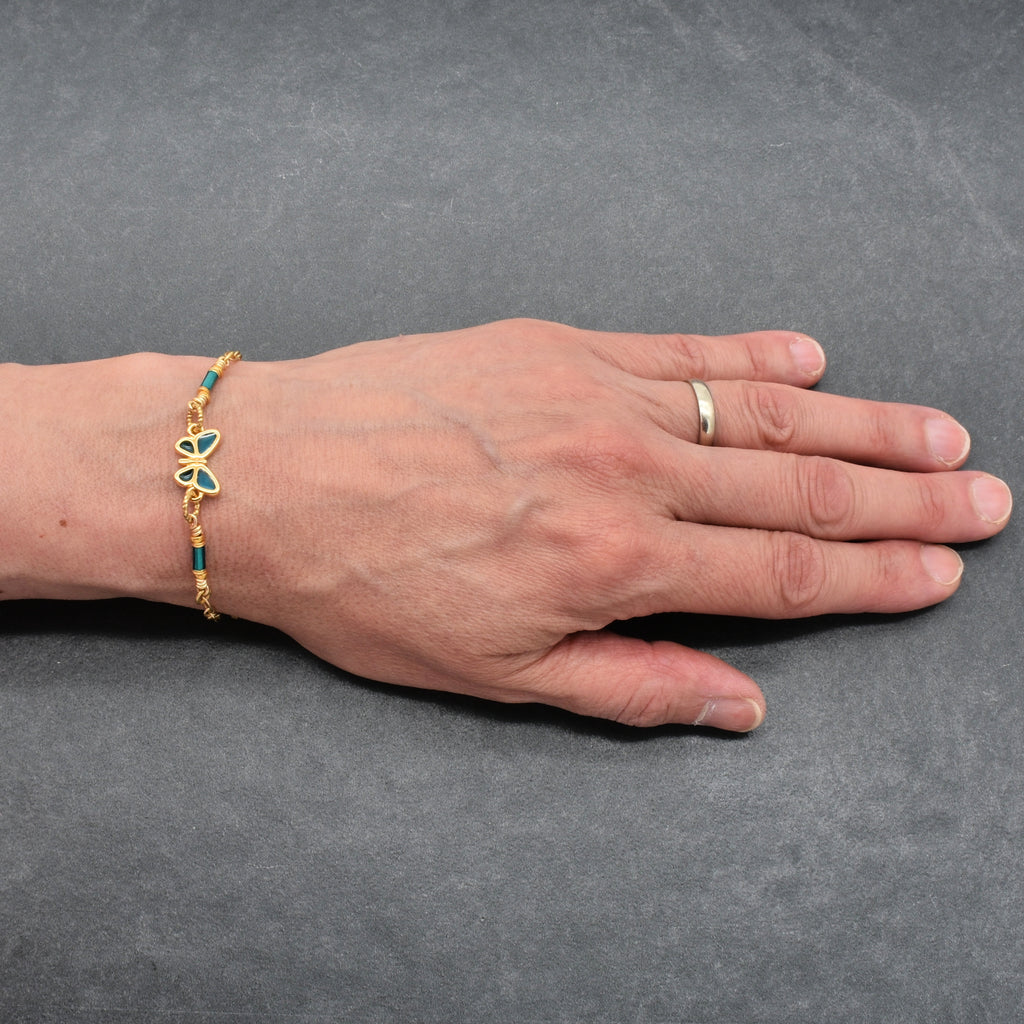 Hand wearing a gold bracelet with a blue butterfly charm on a gray background - wearable art by Ruby Acorn