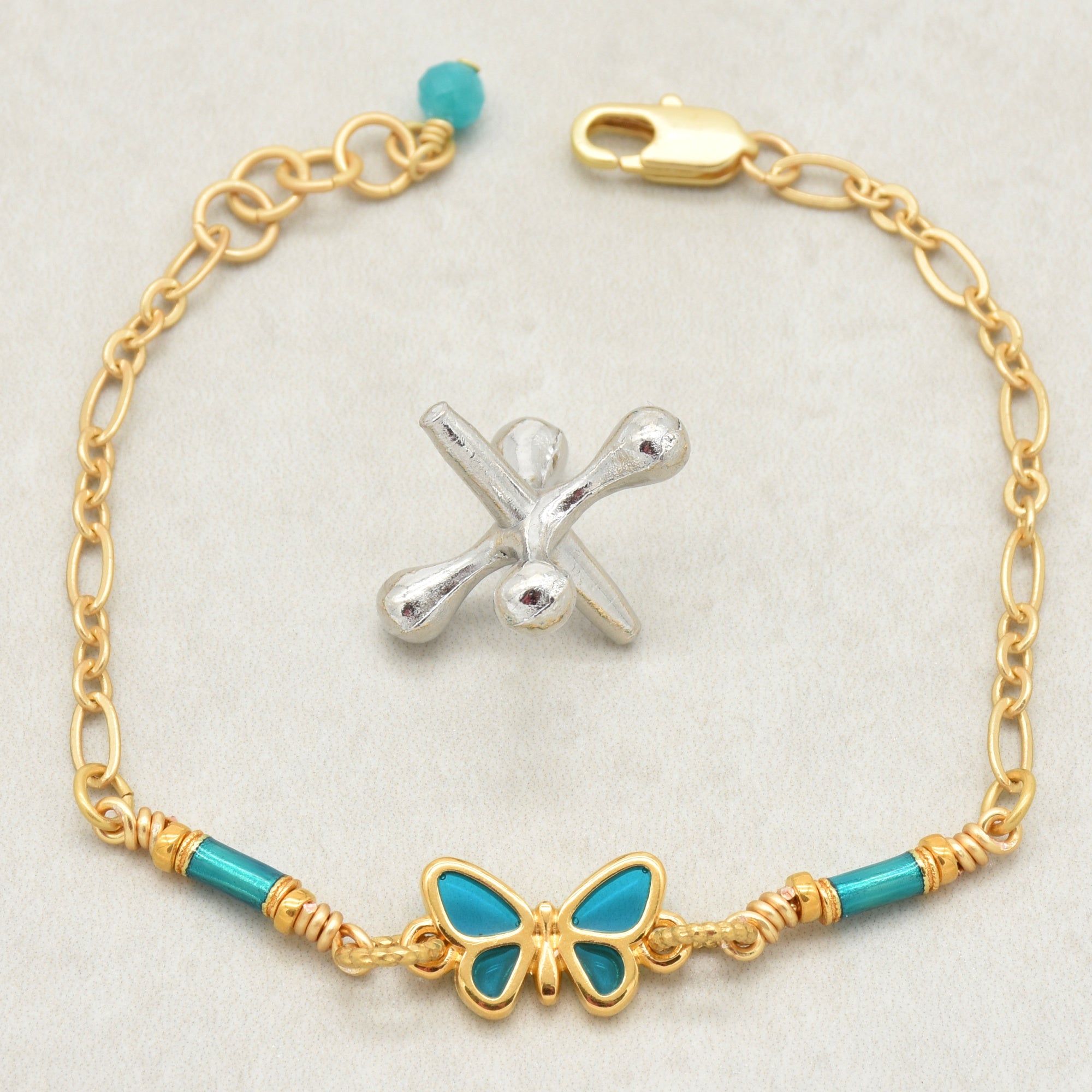 Gold bracelet with turquoise beads and a butterfly charm on a light gray background - wearable art by Ruby Acorn