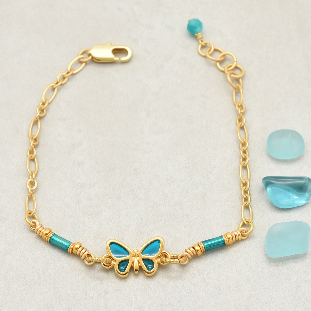 Gold bracelet with blue butterfly charm and beads on a light gray background - one of a kind by Ruby Acorn