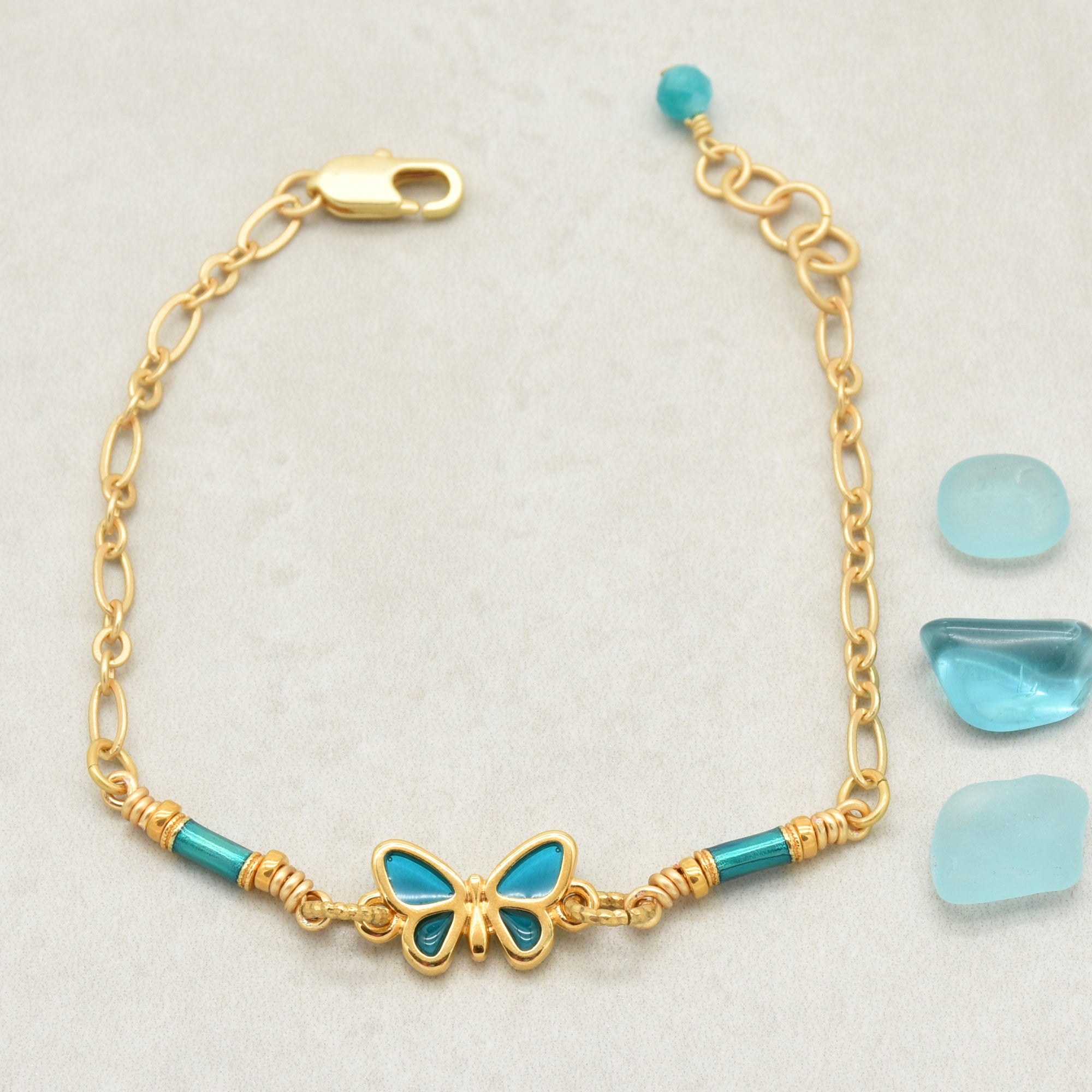 Gold bracelet with blue butterfly charm and beads on a light gray background - one of a kind by Ruby Acorn
