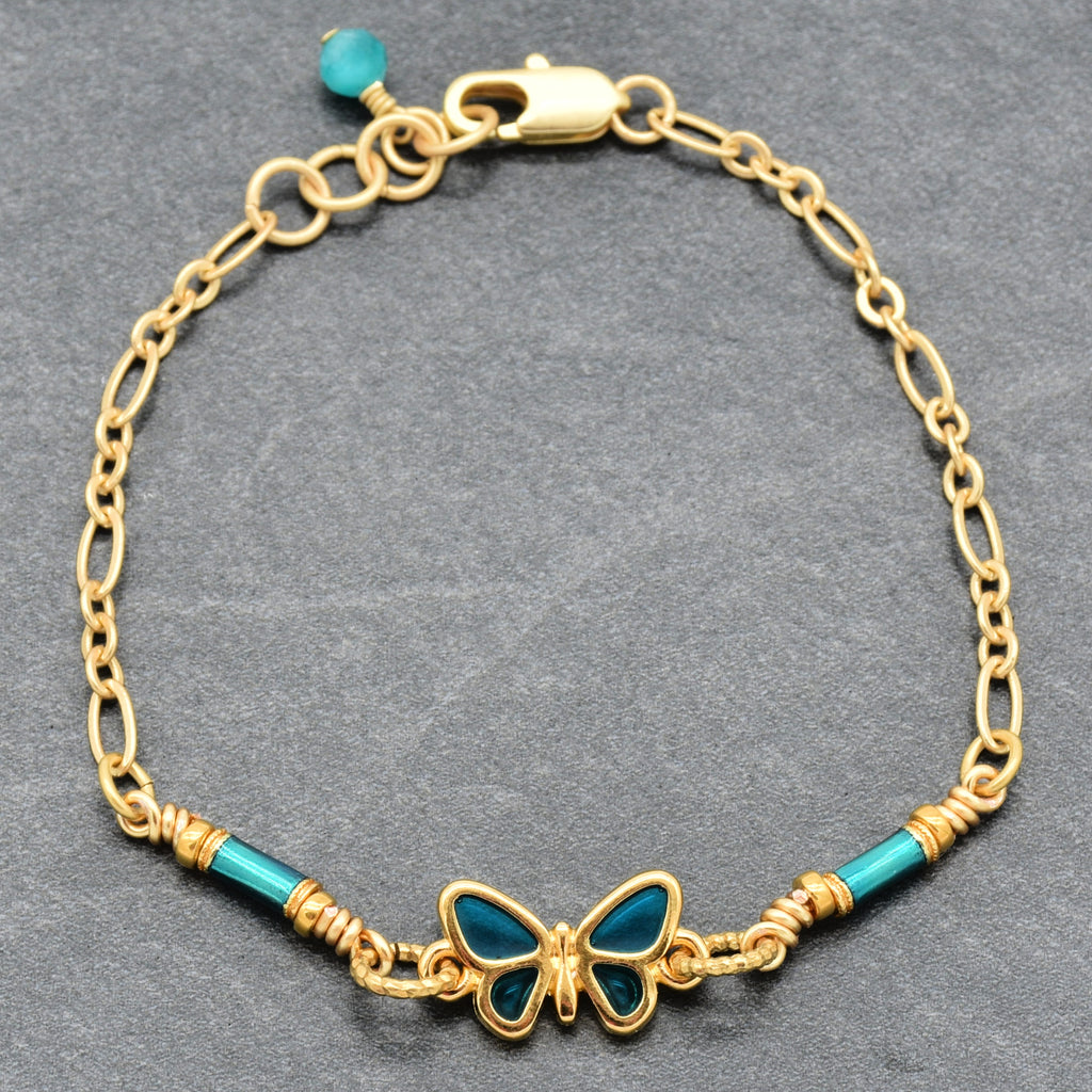Gold bracelet with blue butterfly charm on a gray background - whimsical wearable art by Ruby Acorn