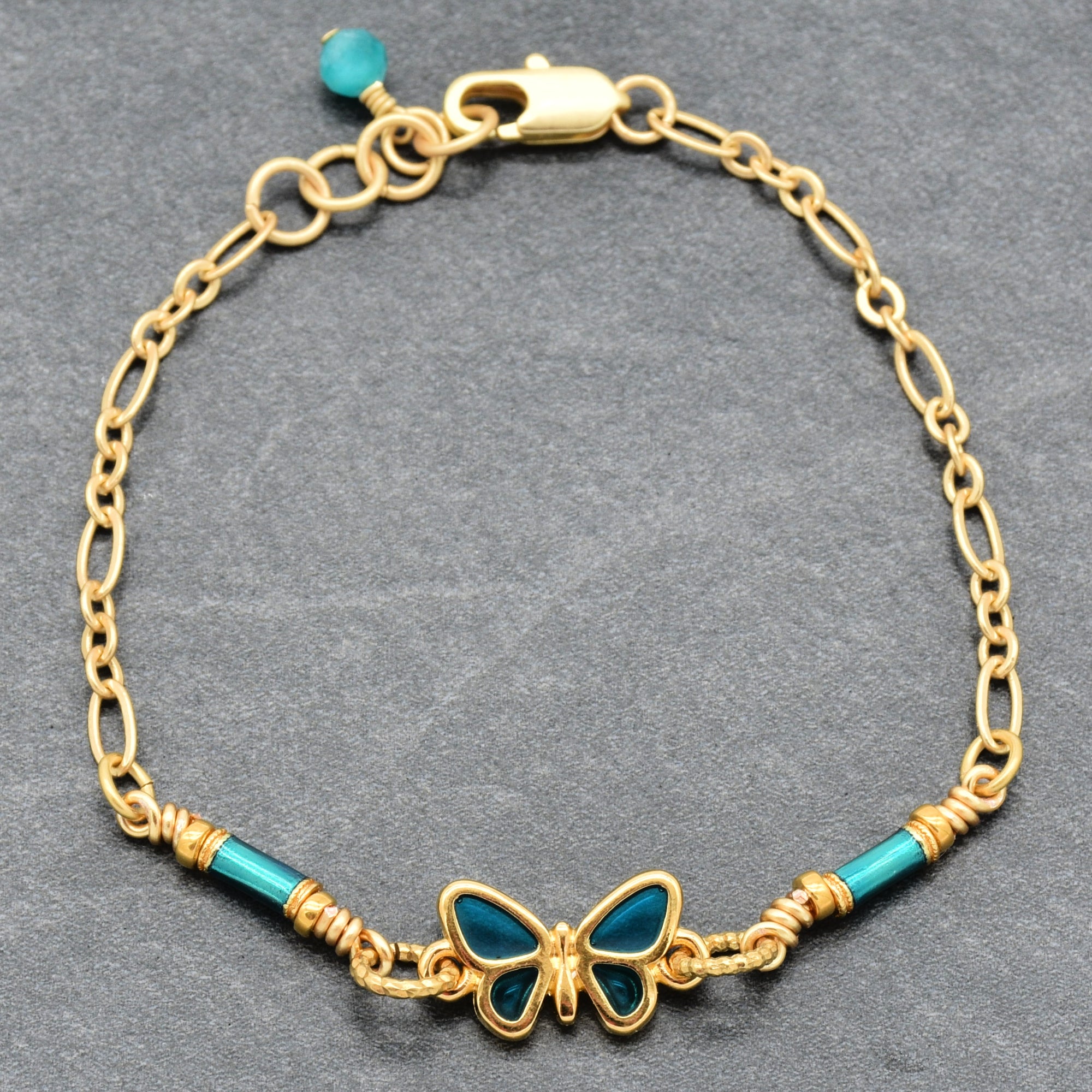Gold bracelet with blue butterfly charm on a gray background - whimsical wearable art by Ruby Acorn