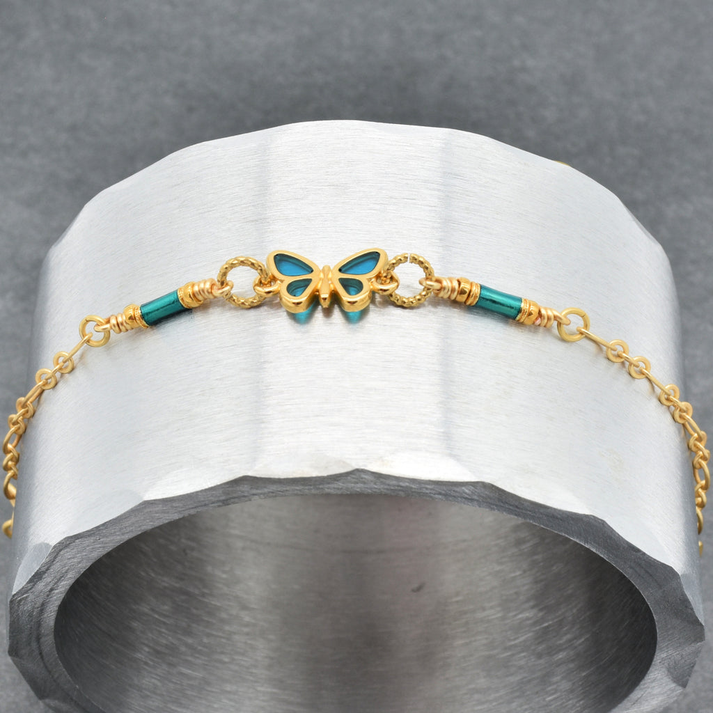 Bracelet with gold chain and blue butterfly charm on a gray stone surface - wearable art by Ruby Acorn