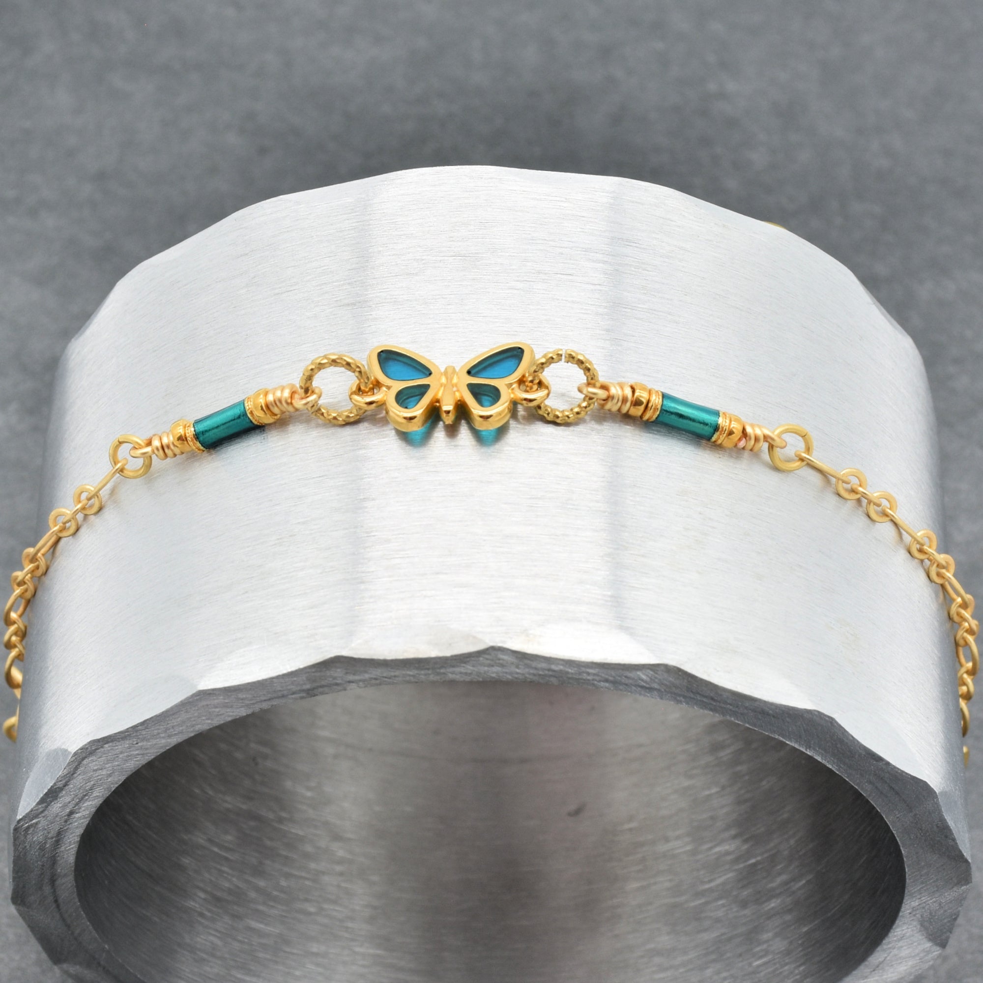 Bracelet with gold chain and blue butterfly charm on a gray stone surface - wearable art by Ruby Acorn