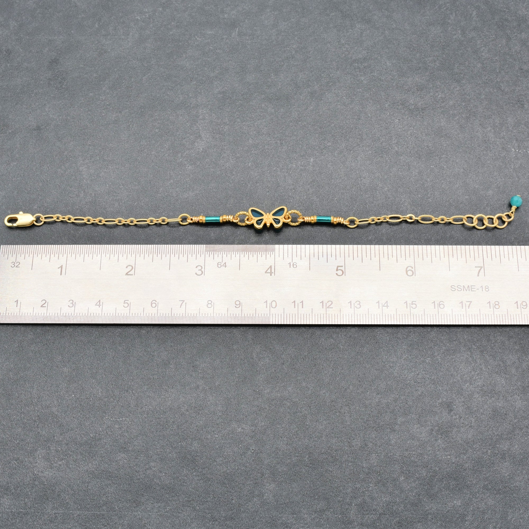 Gold bracelet with blue beads on a gray surface next to a ruler for size reference - Ruby Acorn one of a kind wearable art