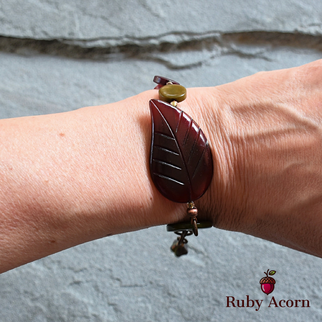 This image shows a bracelet. It is worn around the wrist and features a leaf-shaped decorative element along with other beads.
