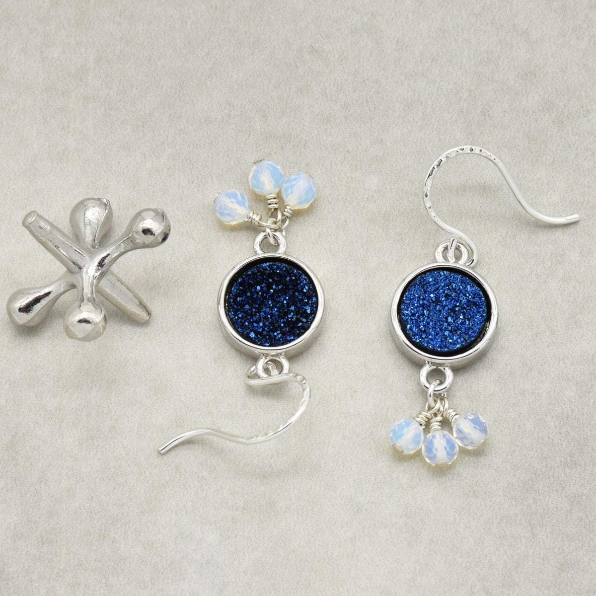 A pair of handmade sterling silver earrings featuring round indigo crystal druzy links and small opalite charms, on a light background.