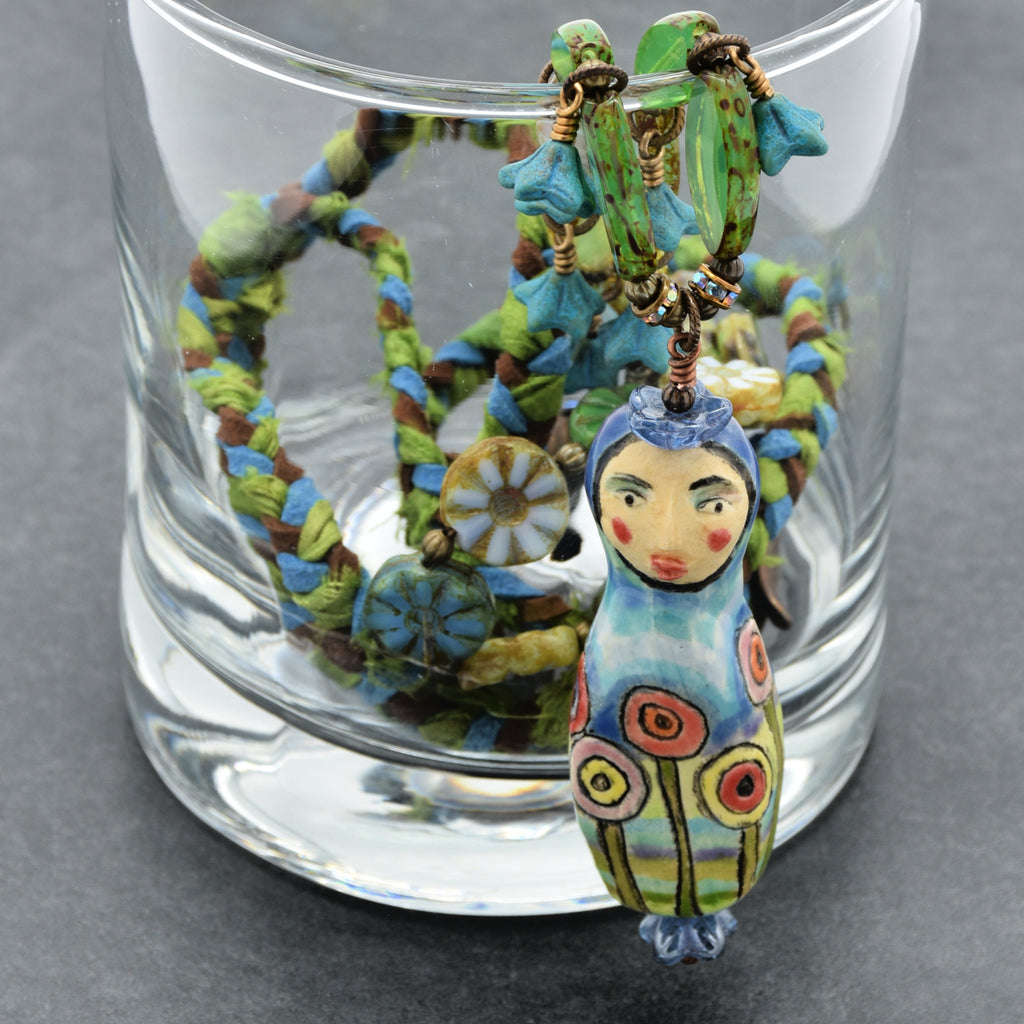 Colorful necklace with a figurine pendant inside a glass container on a gray background