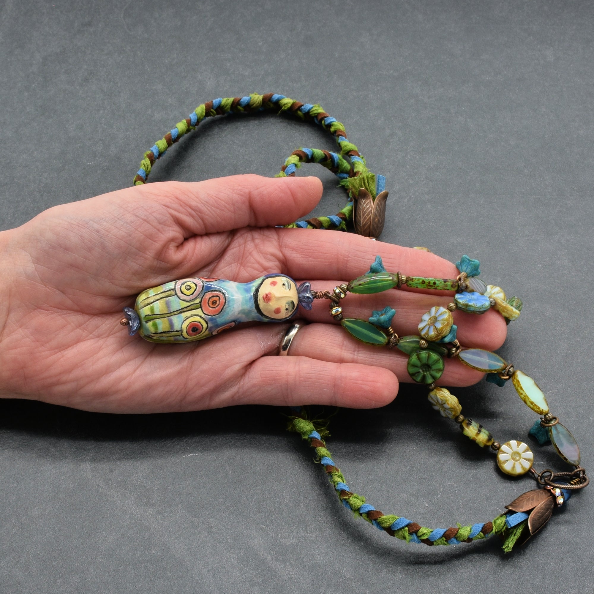 Colorful beaded necklace held in a hand against a gray background