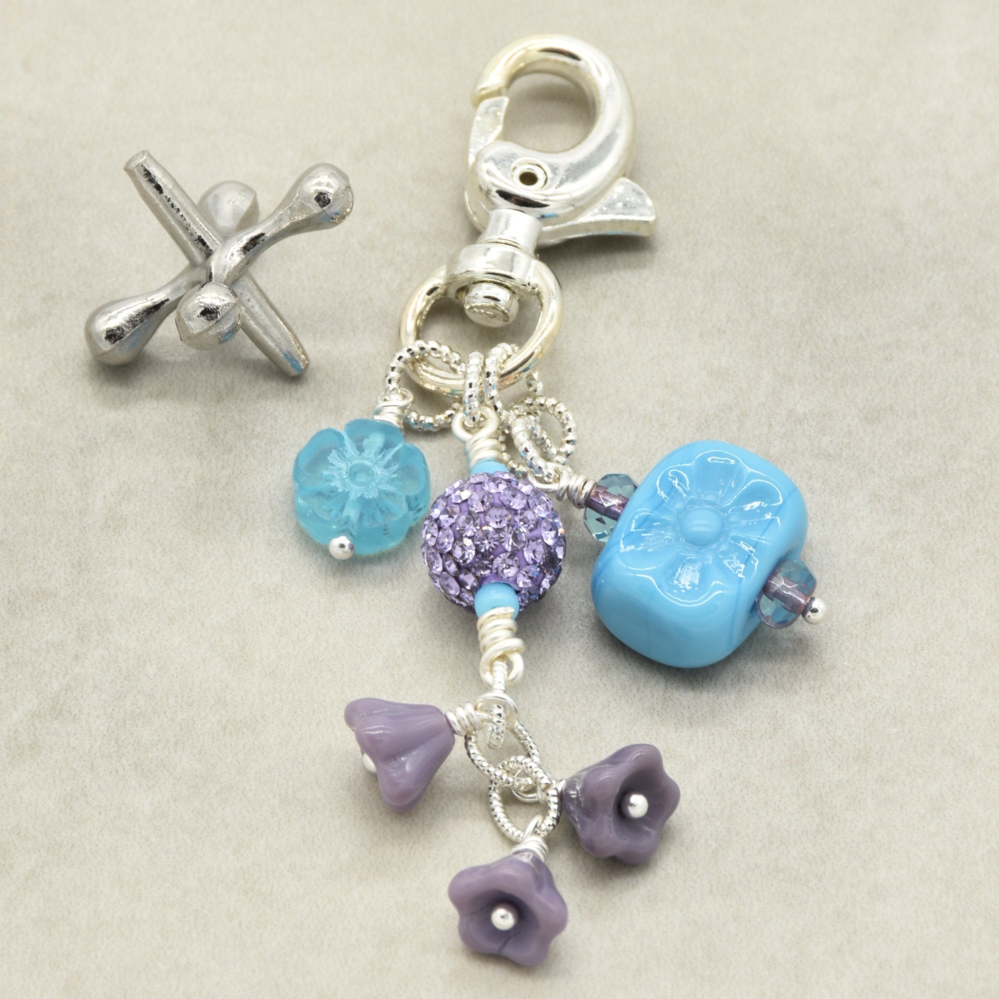 Silver charm with blue and purple beads on a beige background