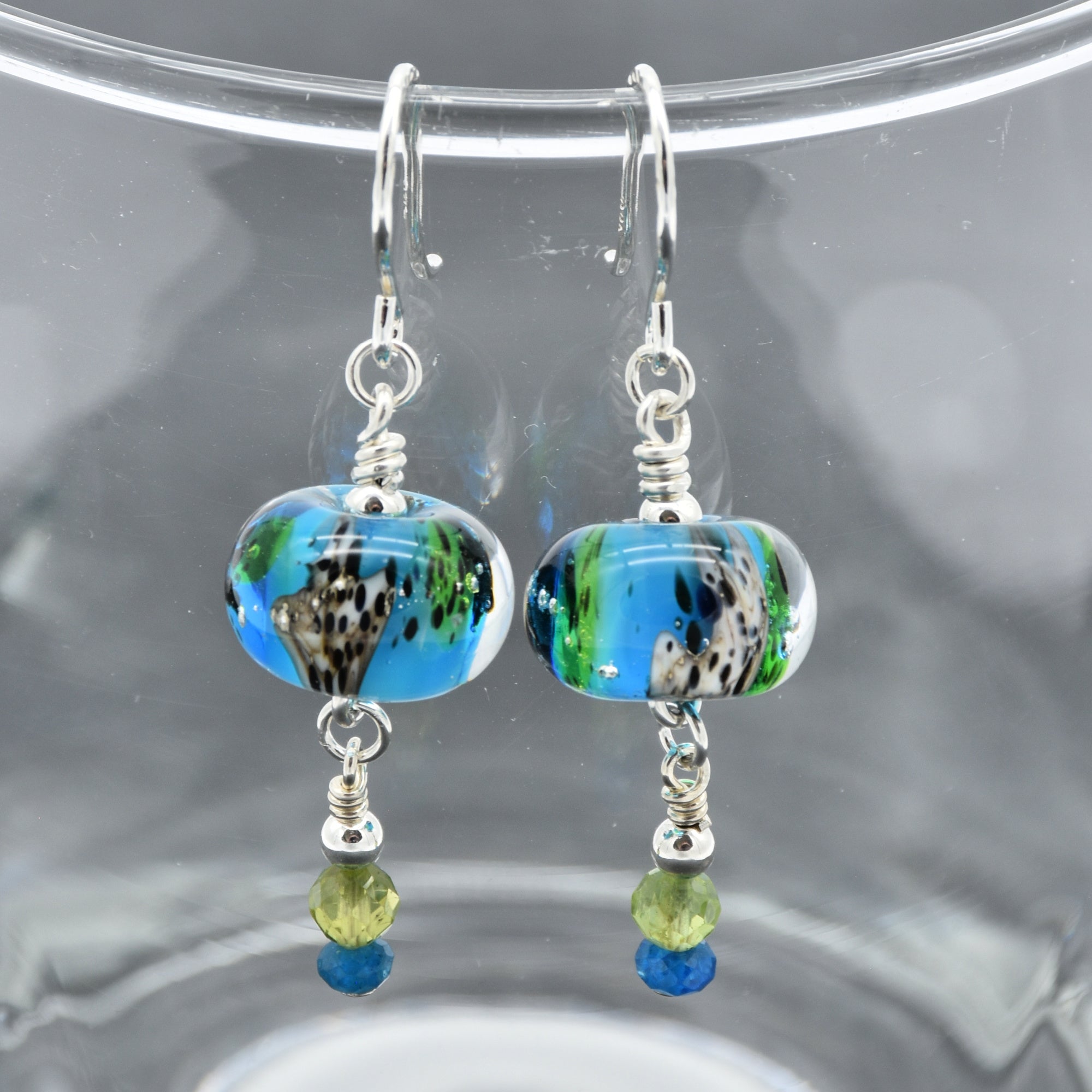 Colorful artisan lampwork glass earrings with sterling silver ear wires, peridot and apatite on a glass surface - handmade with love by Ruby Acorn