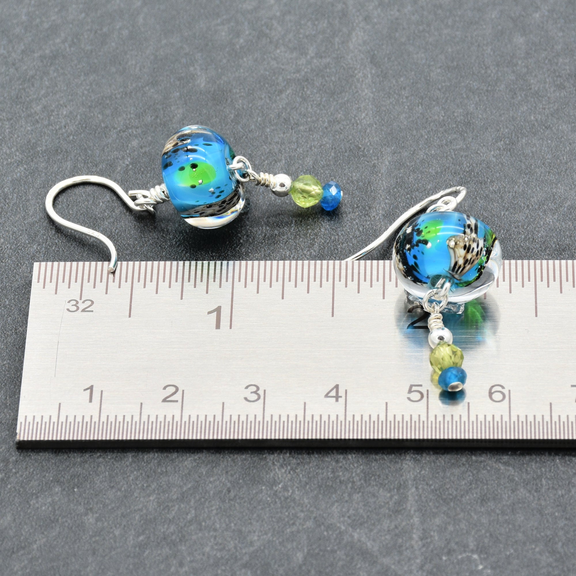 Colorful artisan lampwork glass earrings with sterling silver ear wires, peridot and apatite beside a ruler for scale - handmade with love by Ruby Acorn