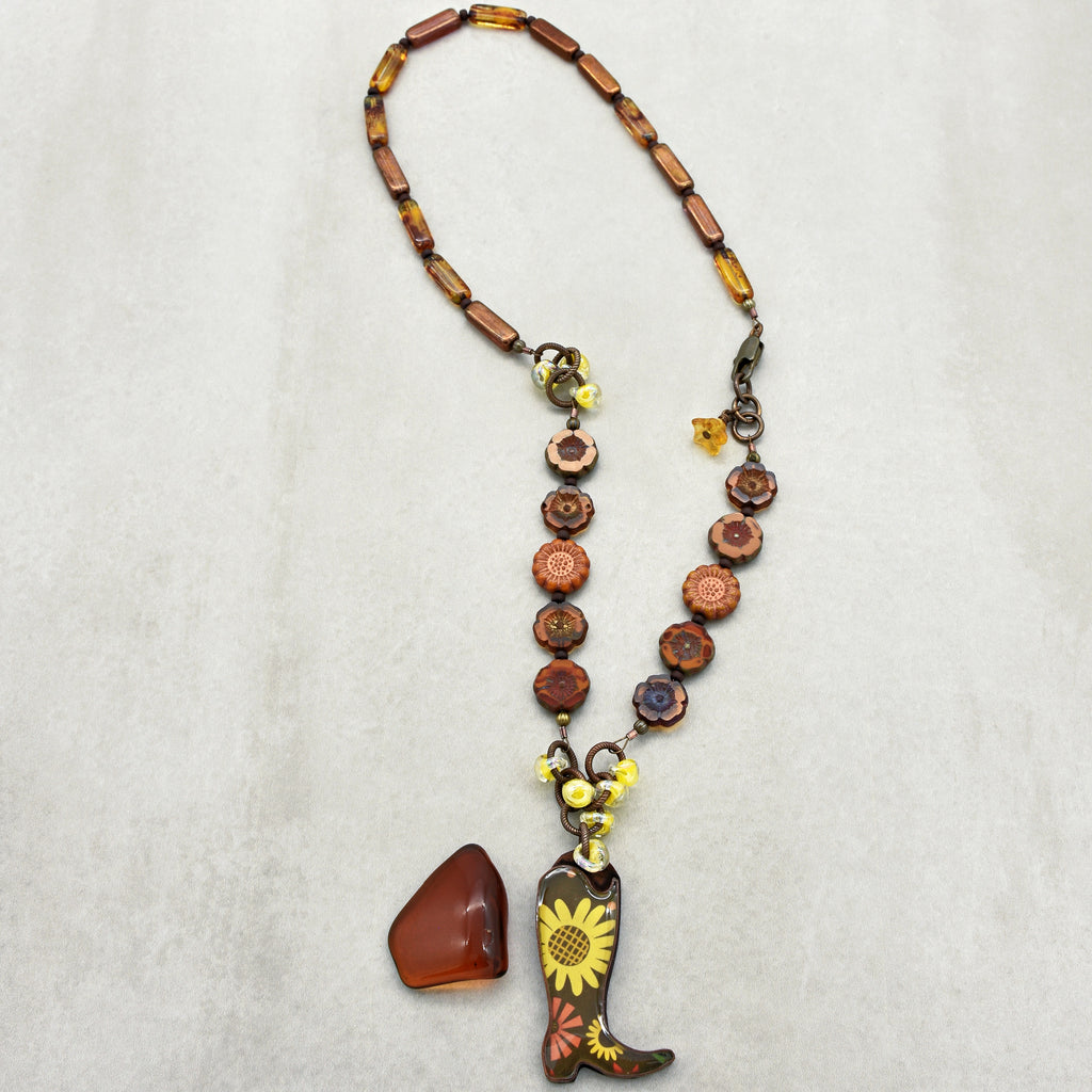 Necklace with cowboy boot and sunflower pendant on a light gray background