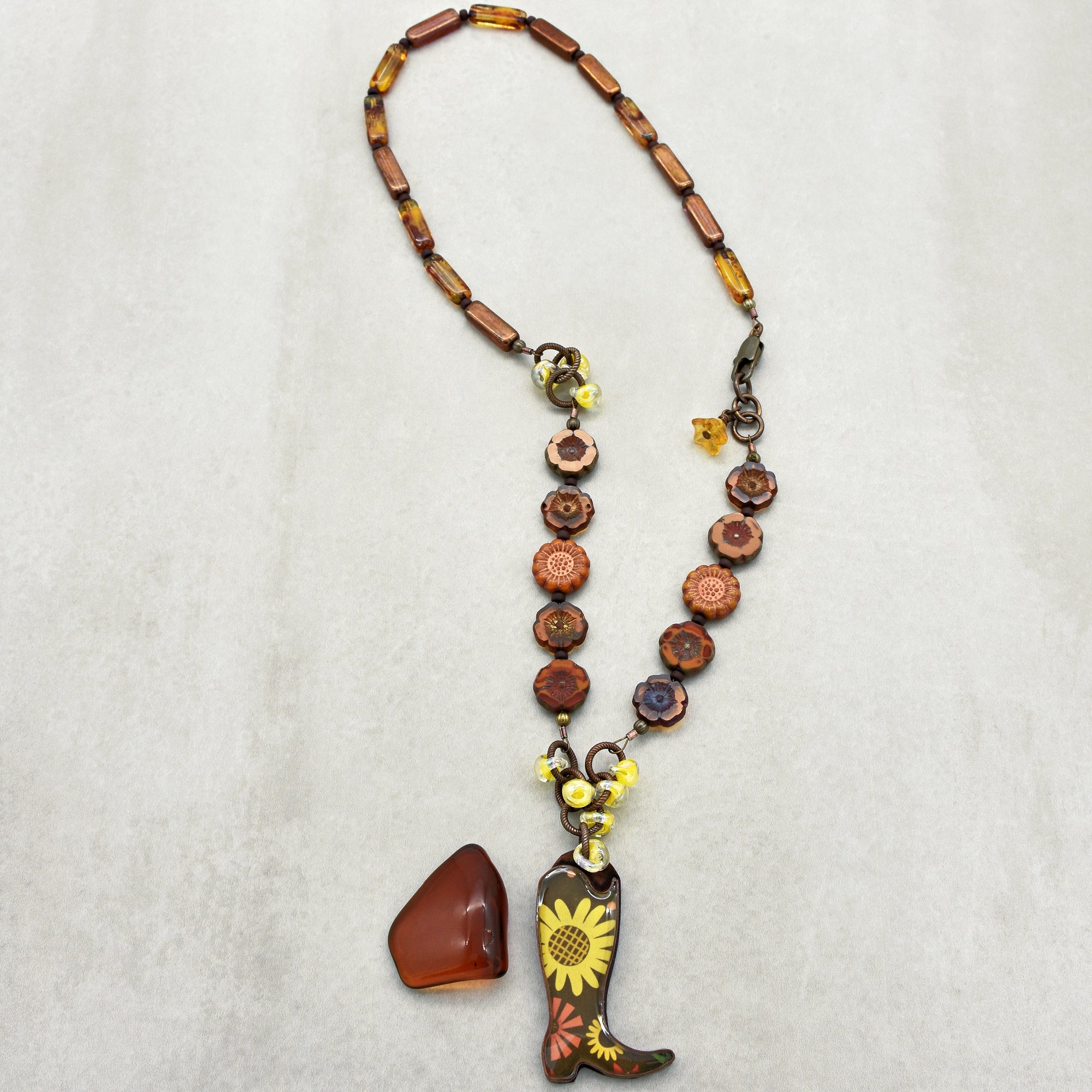 Necklace with cowboy boot and sunflower pendant on a light gray background