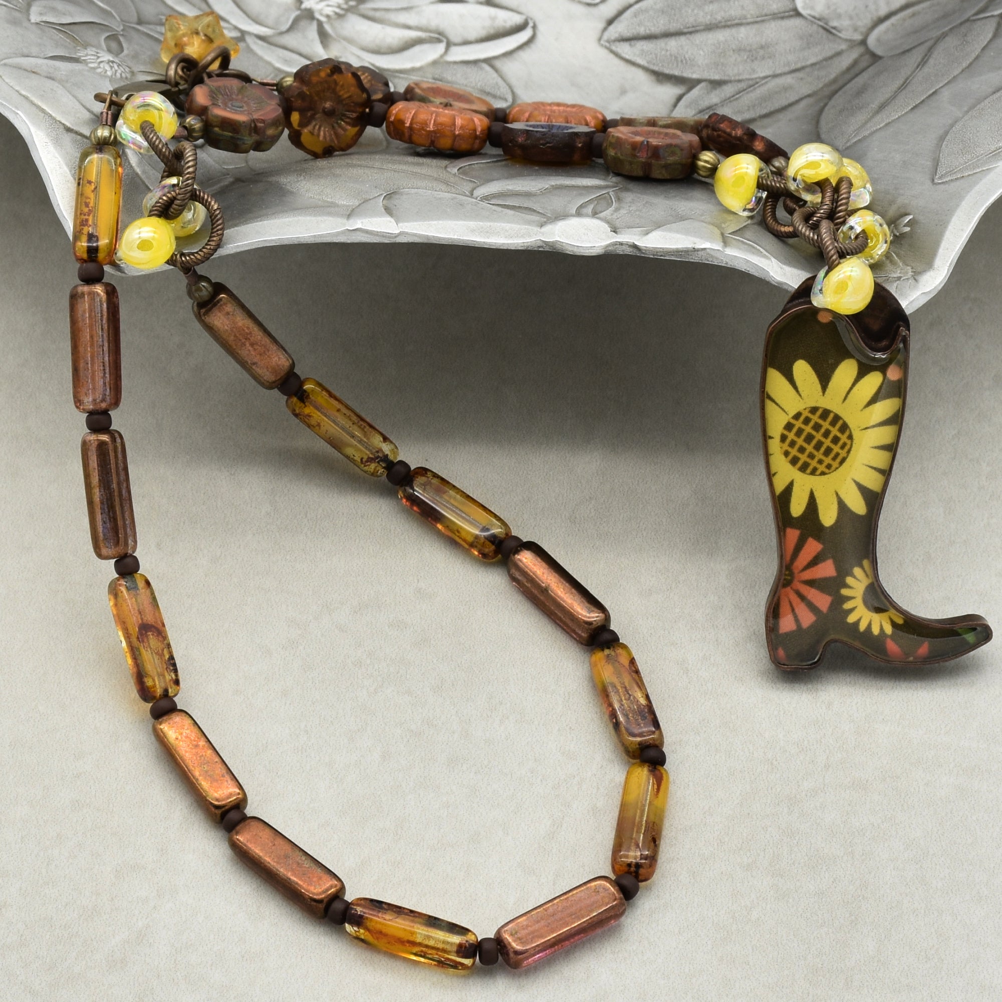 Necklace with brown and yellow beads on a decorative boot with floral design.