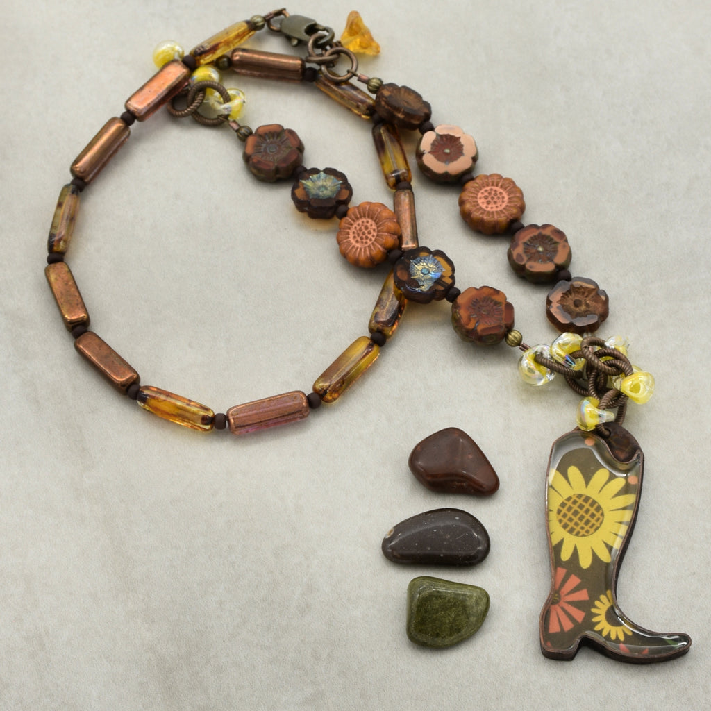 Necklace with cowboy boot and sunflower charm on a light background