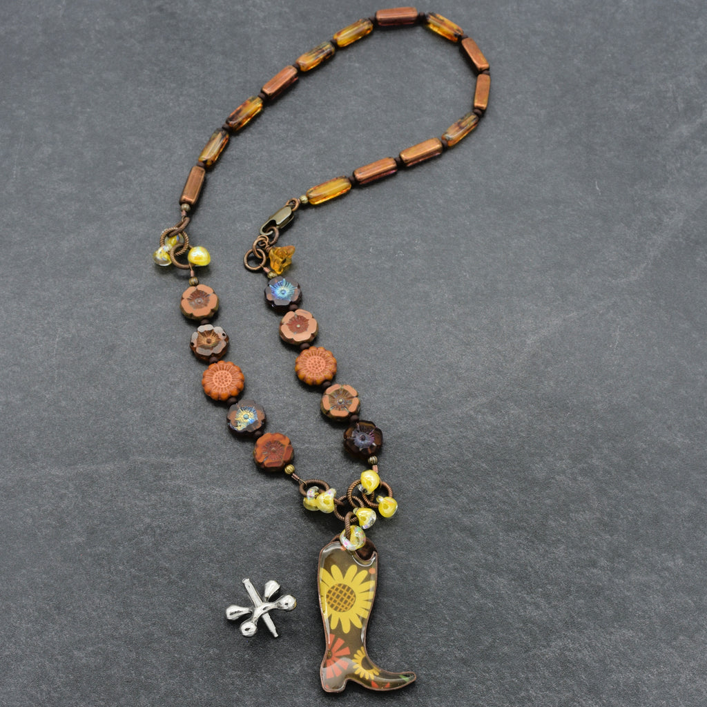 Necklace with cowboy boot charm and sunflower pendant on a gray background