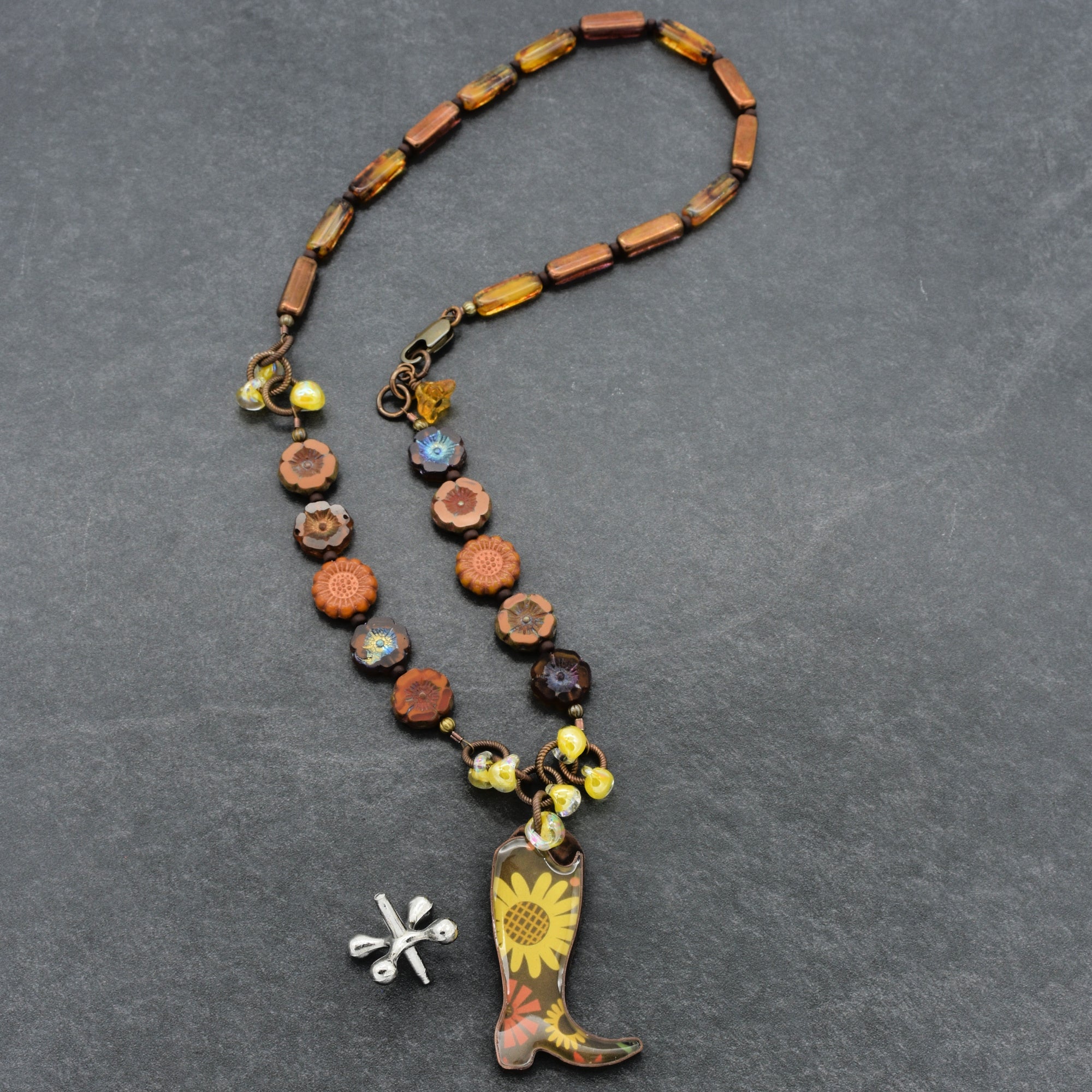 Necklace with cowboy boot charm and sunflower pendant on a gray background