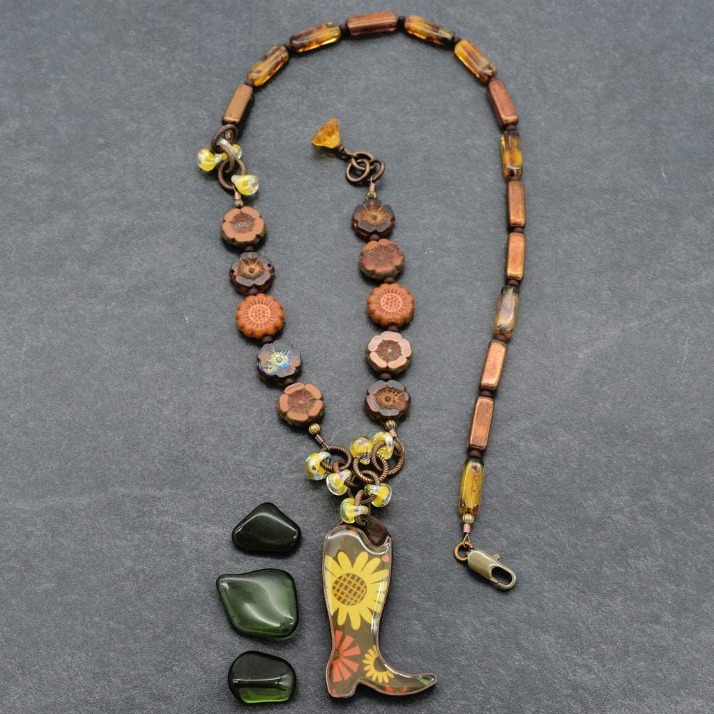 Necklace with cowboy boot and sunflower pendant on a gray background
