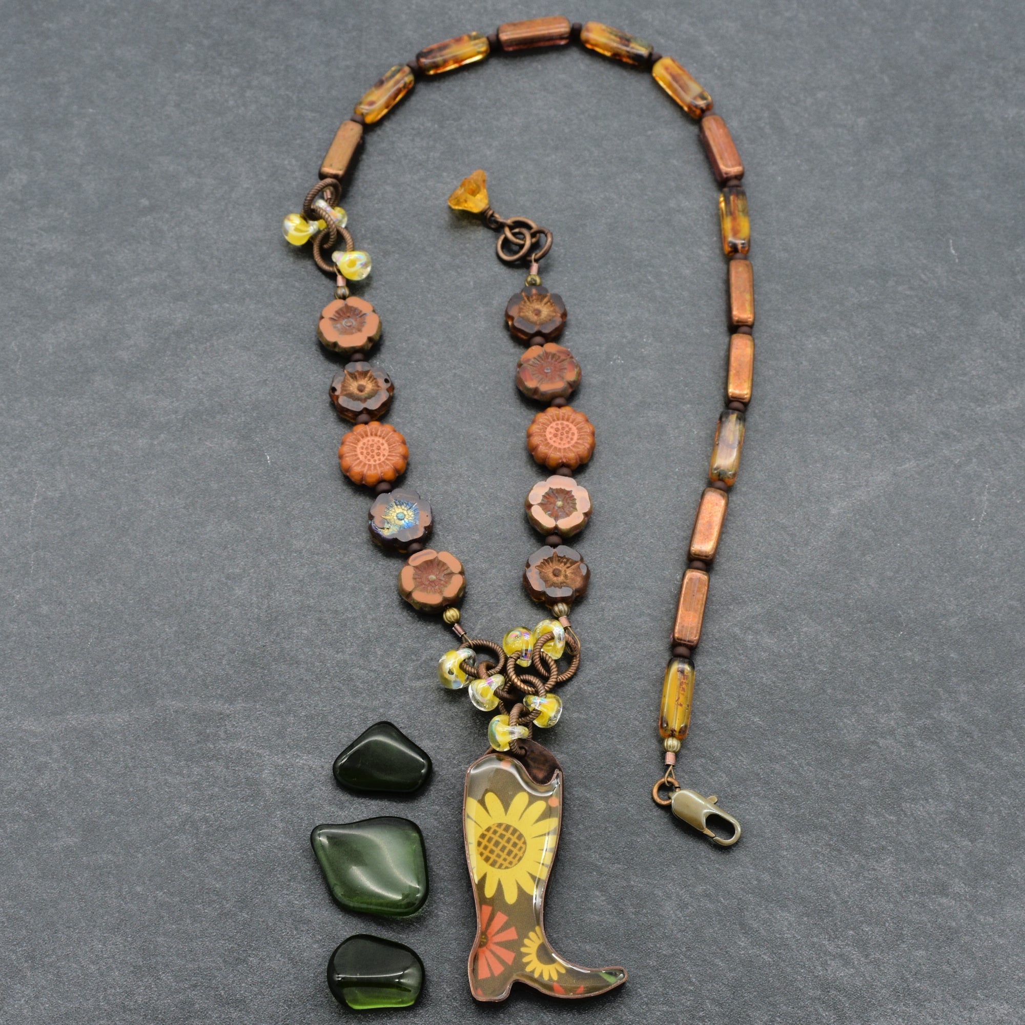 Necklace with cowboy boot and sunflower pendant on a gray background