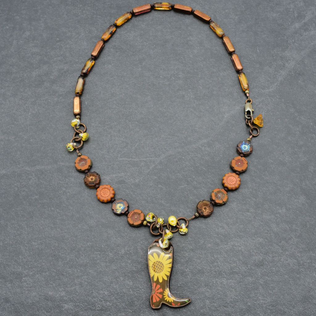 Necklace with cowboy boot pendant and floral design on a gray background
