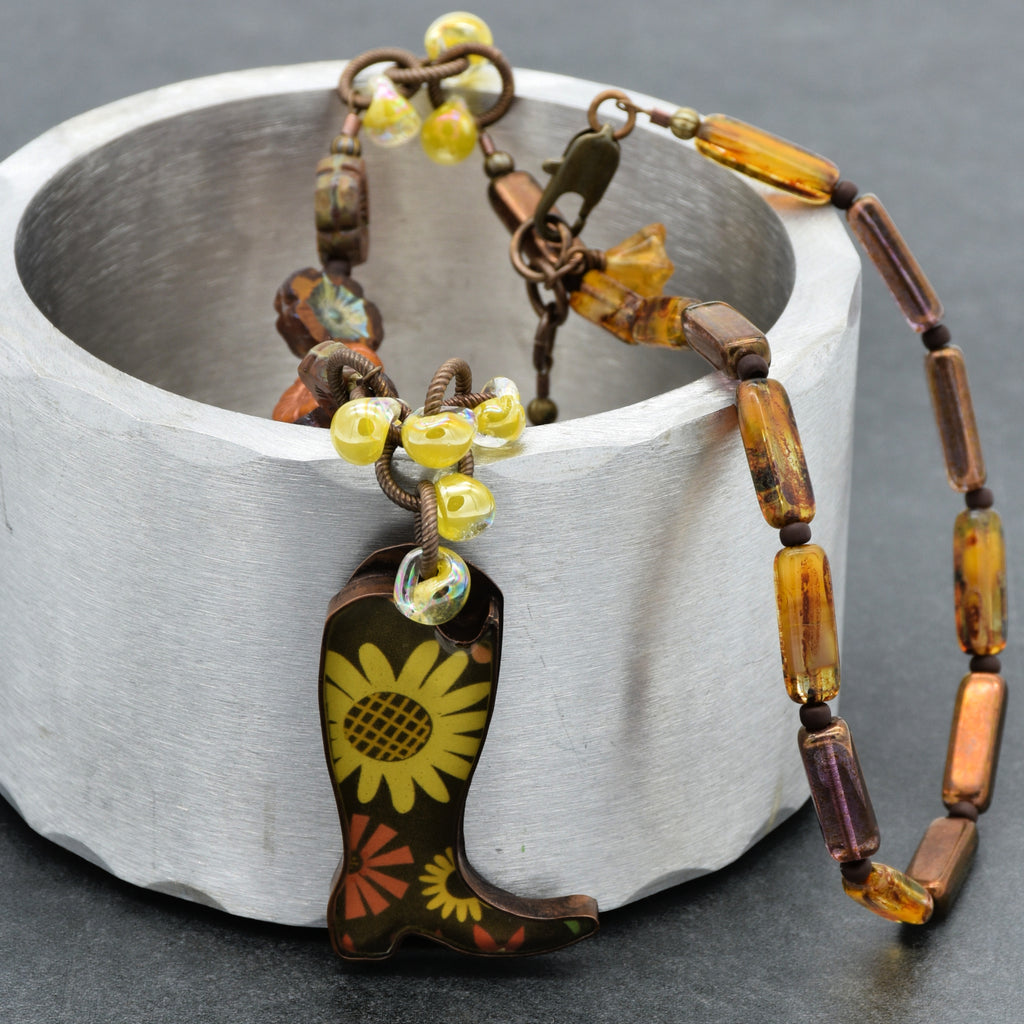 Necklace with cowboy boot pendant and colorful beads on a metallic surface