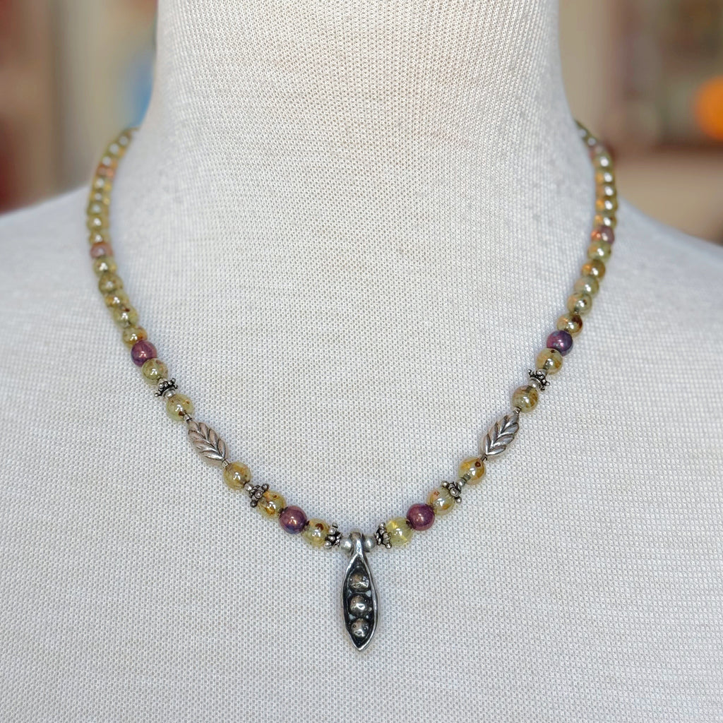 Necklace with multicolored beads and a pewter peapod pendant on a mannequin.
