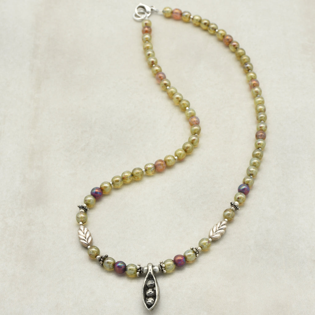 Beaded necklace with pewter peapod shaped pendant on a beige background
