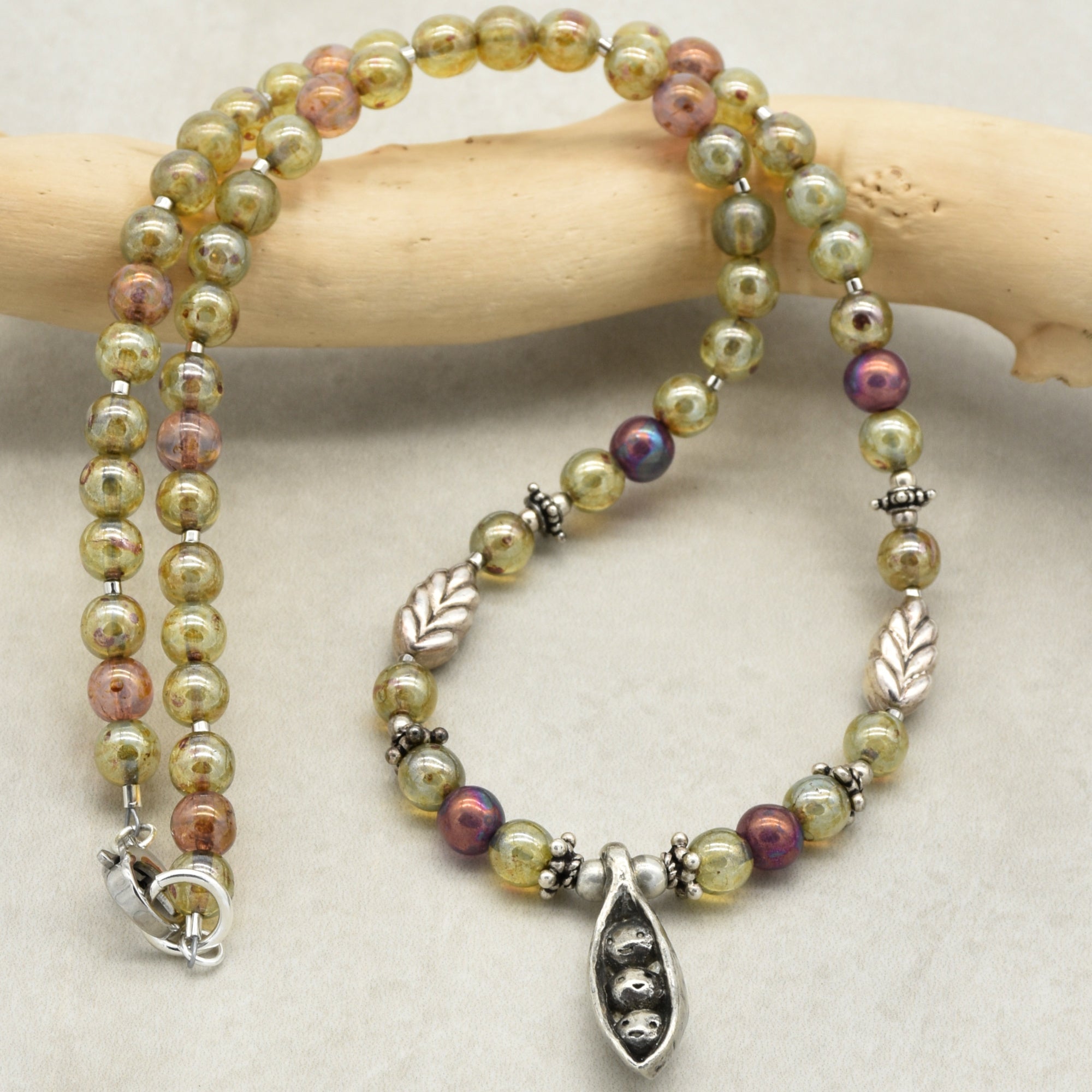 Beaded necklace with a pewter peapod focal on a wooden stick