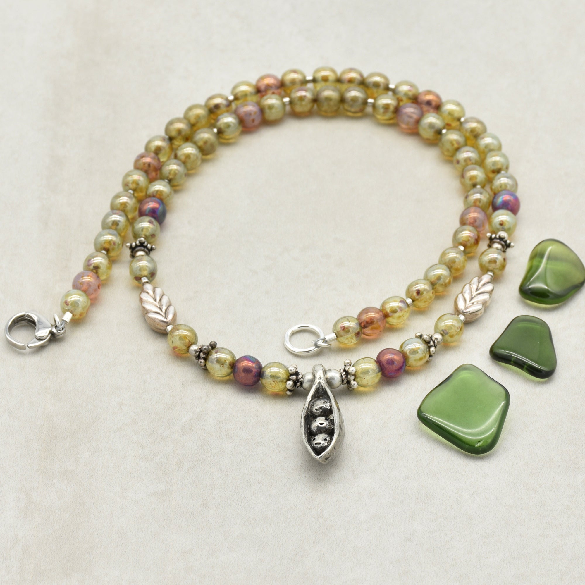 Multicolored beaded necklace with pewter peapod pendant on a light background