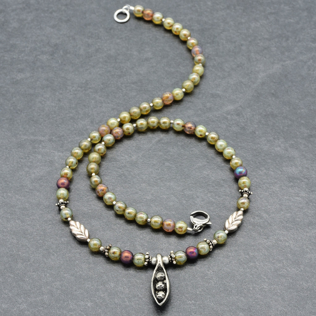 Beaded necklace with silver clasp and pewter peapod pendant on a gray background