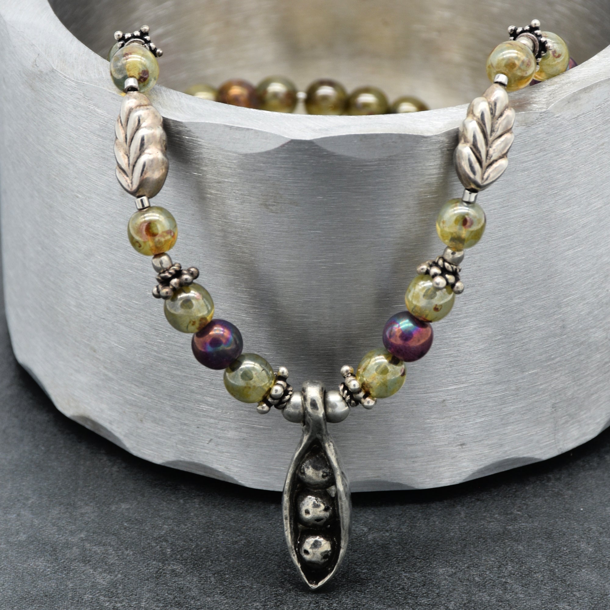 Beaded necklace with peapod-shaped pendant on a metallic surface