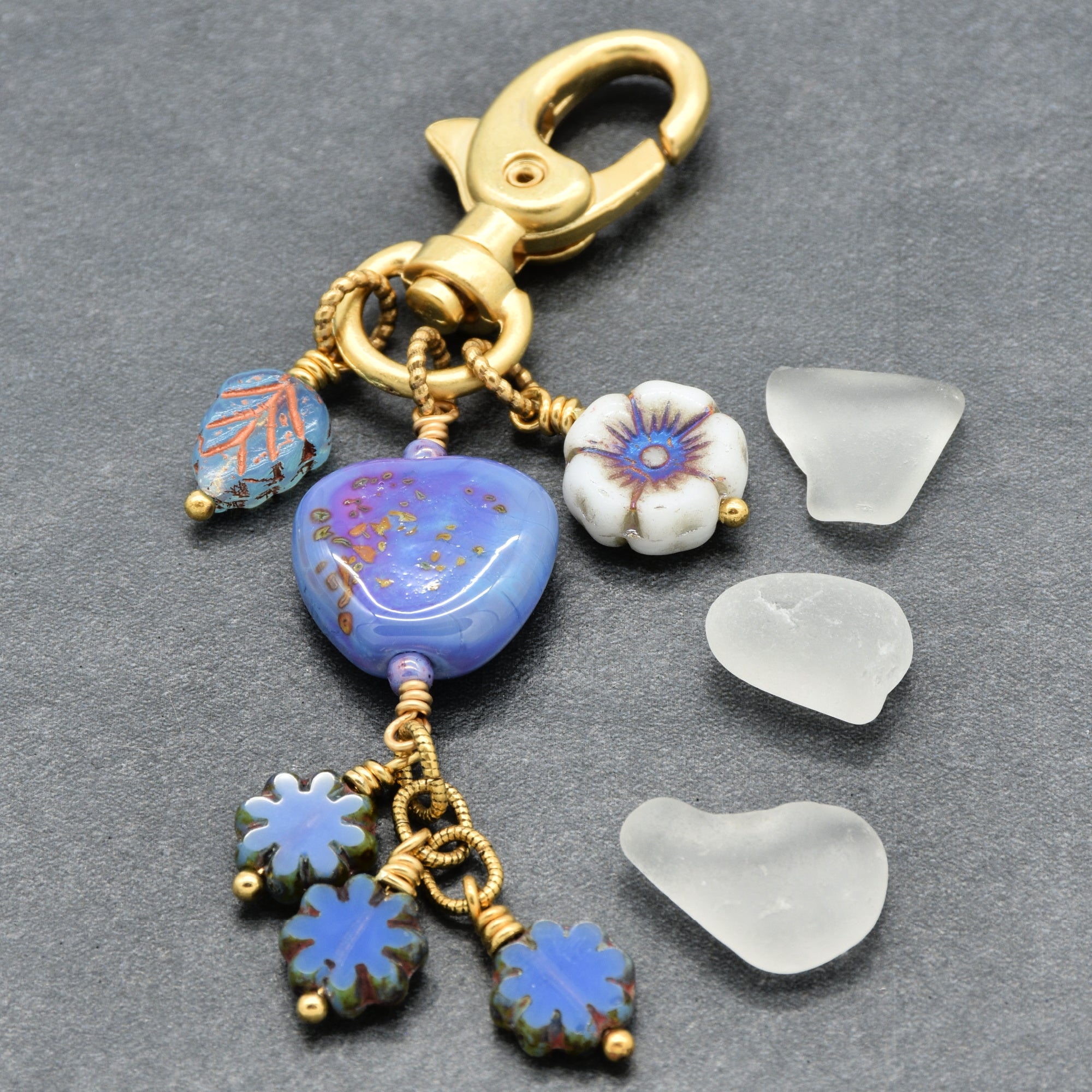 Gold keychain with blue and white floral charms on a gray background