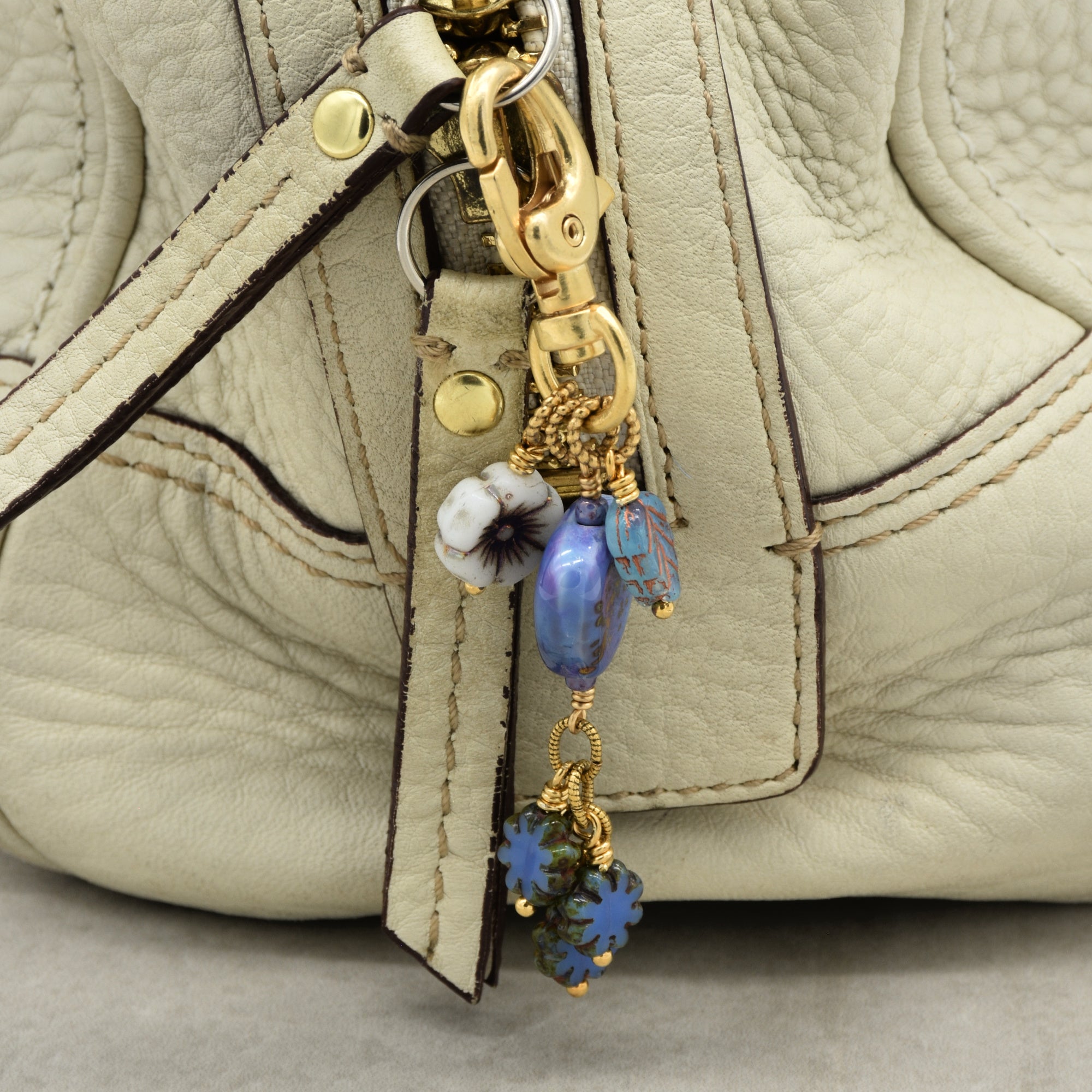 Close-up of a beige handbag with a decorative keychain featuring blue and gold elements.
