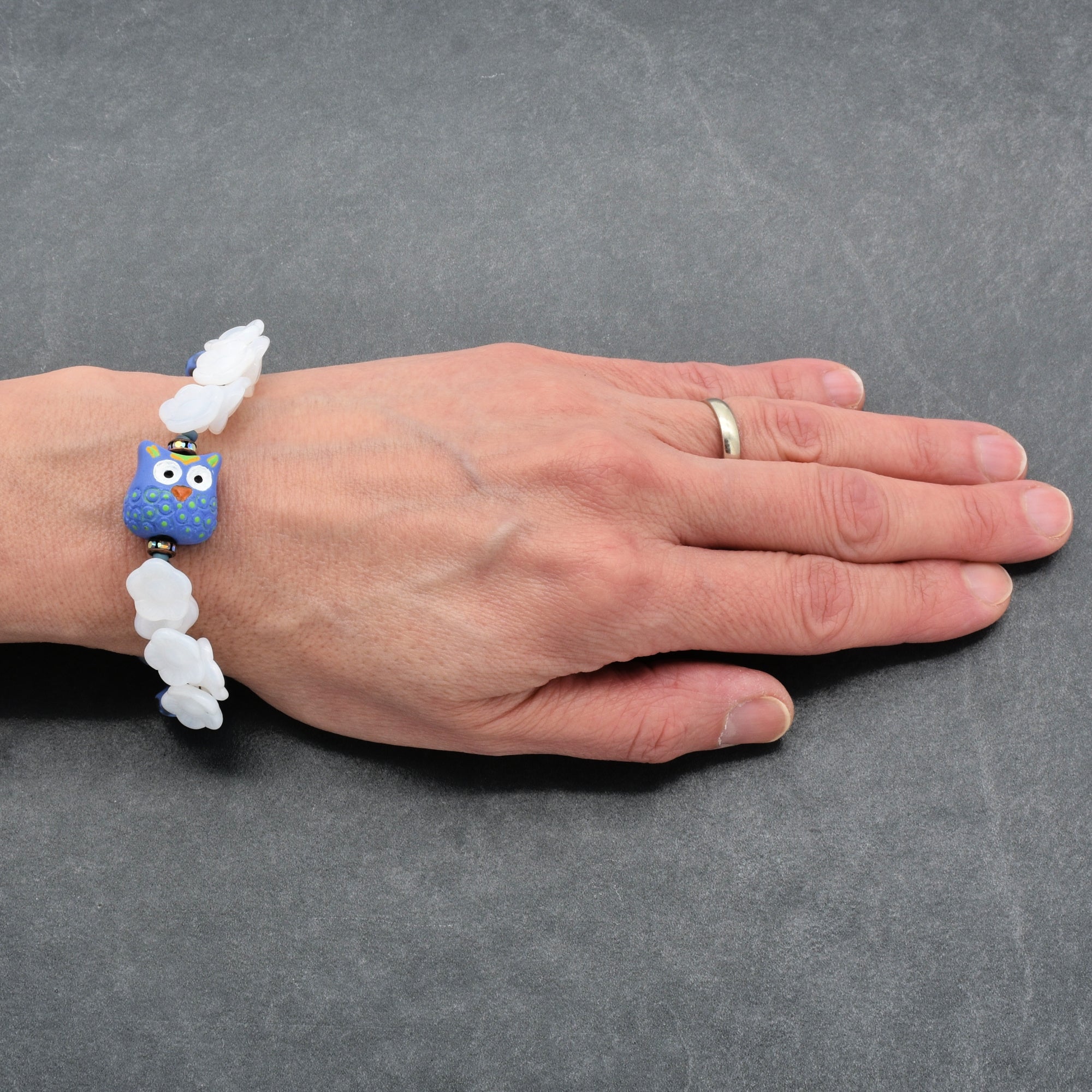 Hand wearing a bracelet with a blue owl focal on a gray background