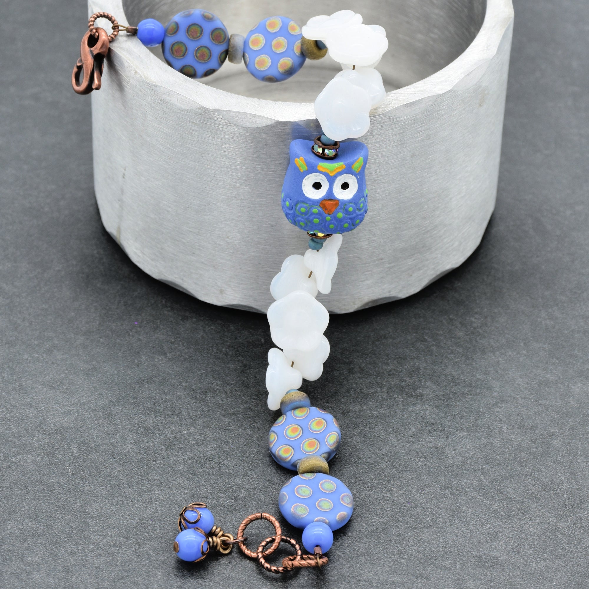 Beaded bracelet with owl focal and blue polka dot beads on a gray background