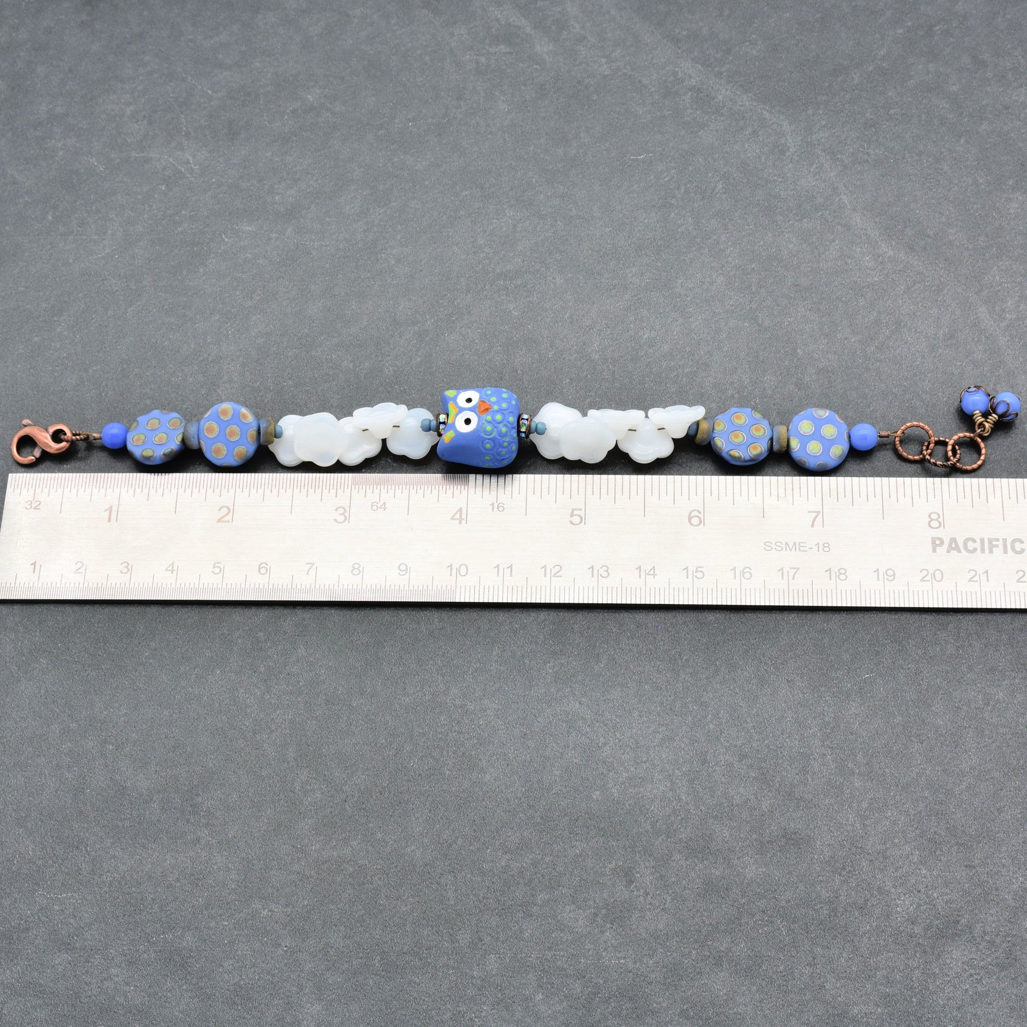 Beaded bracelet with blue and white beads on a gray surface with a ruler for scale.