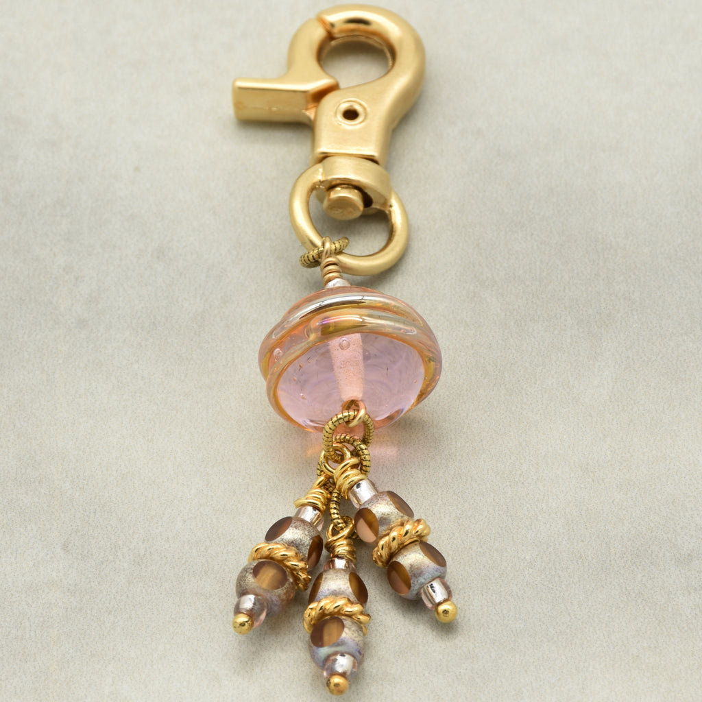 Gold charm with pink bead and dangling beads on a beige background