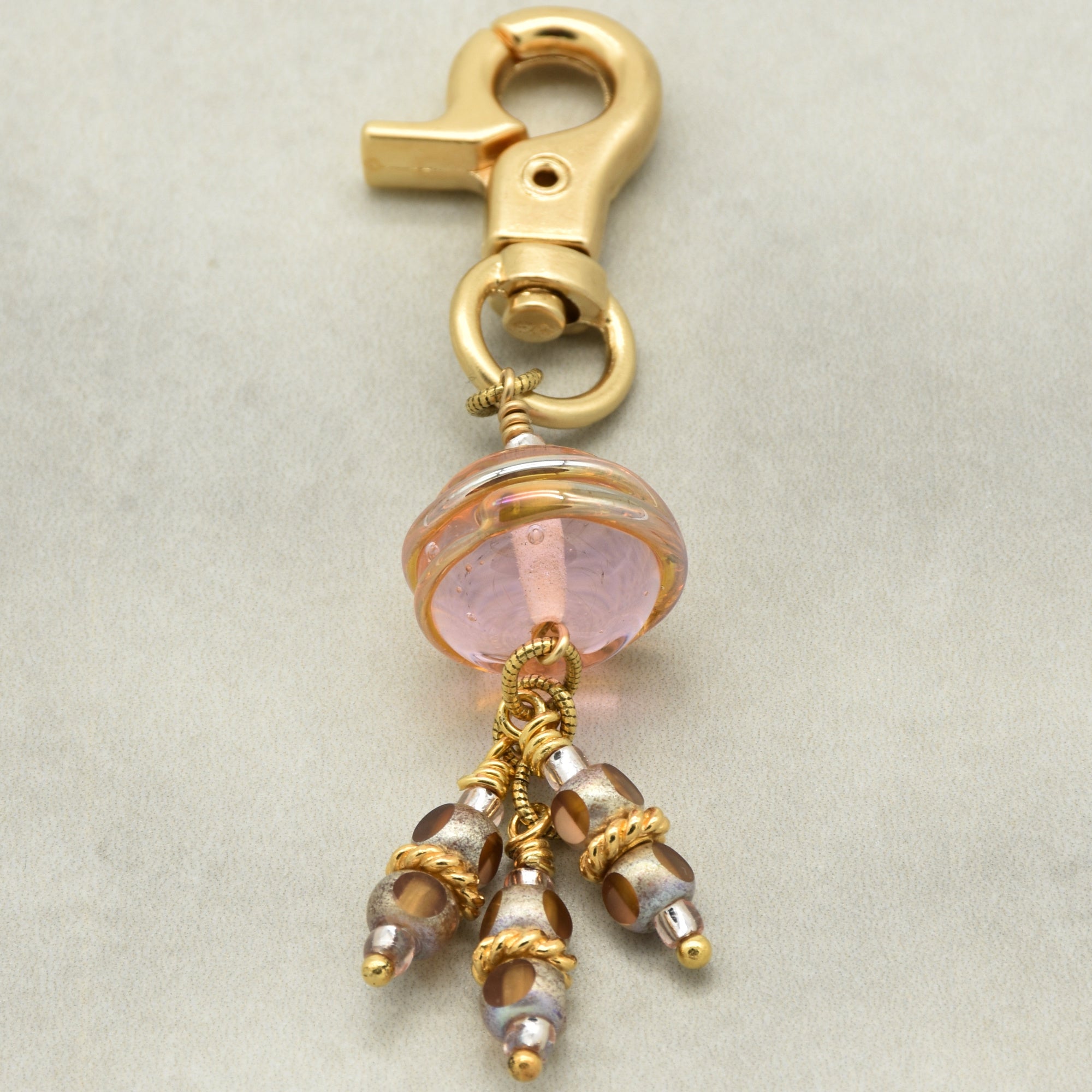 Gold charm with pink bead and dangling beads on a beige background