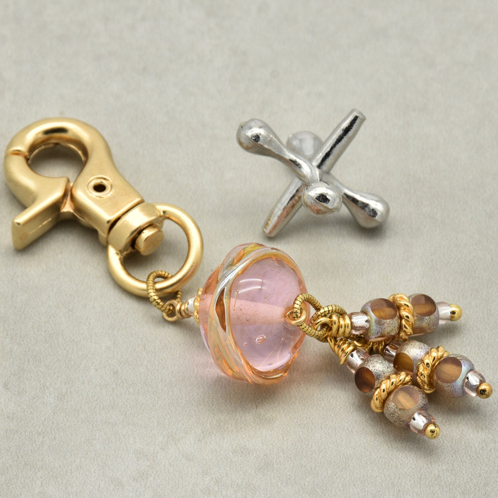Gold keychain with pink glass bead and  ivory beads on a light gray background