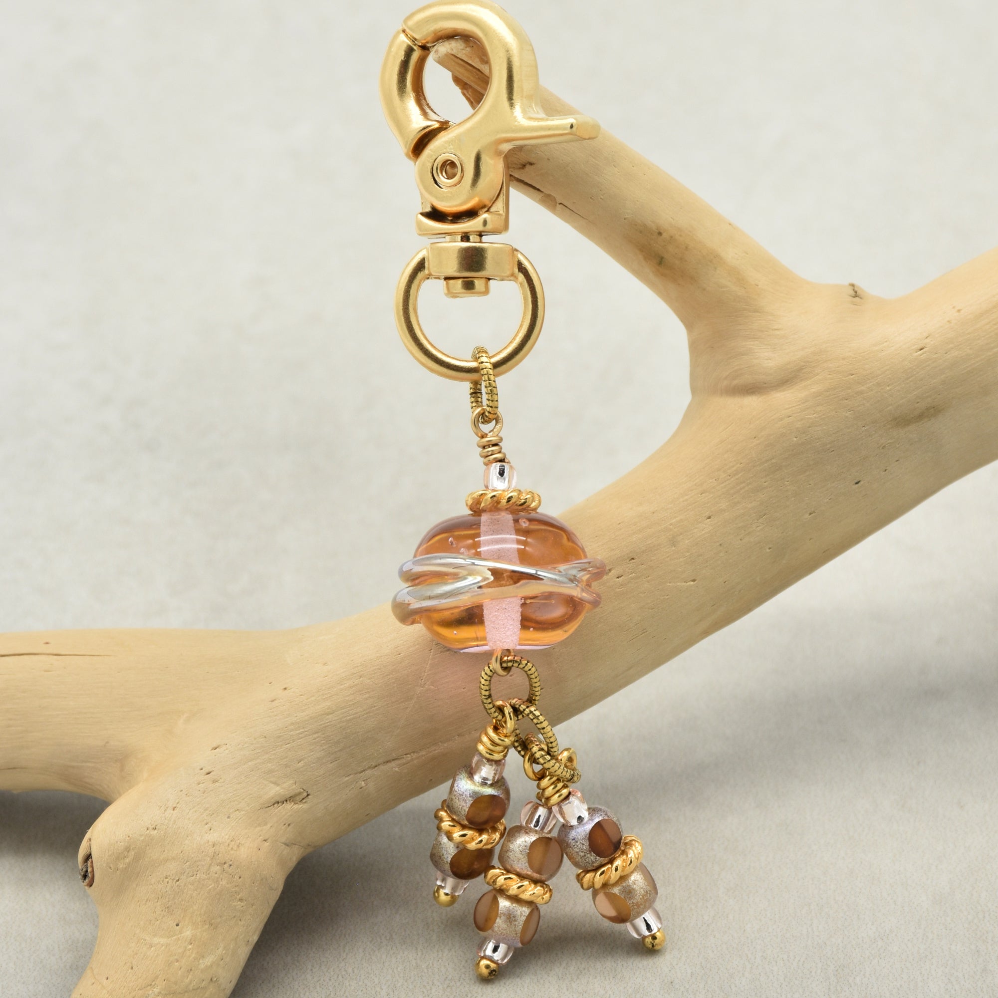 Gold keychain with pink beads on a wooden branch